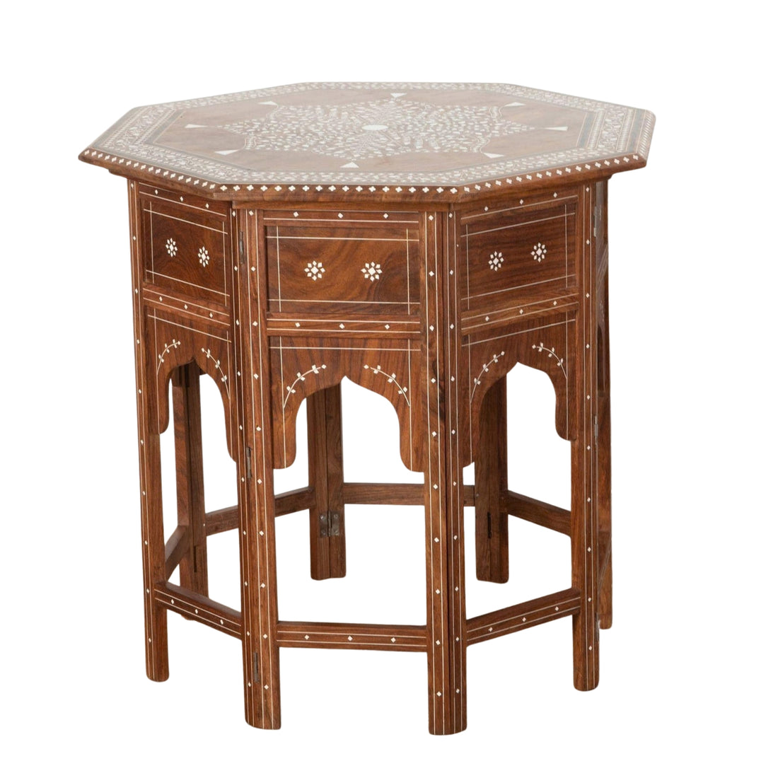 An ornate dark wood writing desk or console table with carved details and brass hardware, styled in a richly decorated bohemian room with rugs, plants, candles, and leather poufs.