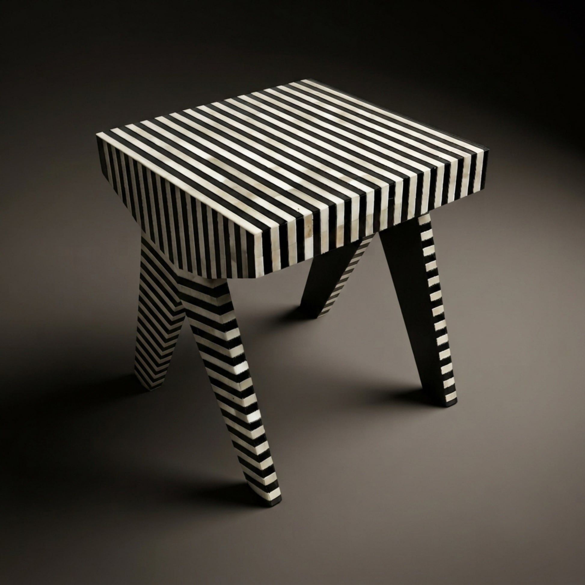 A small stool with a black and white striped pattern on the seat and legs, photographed on a dark gray studio background.