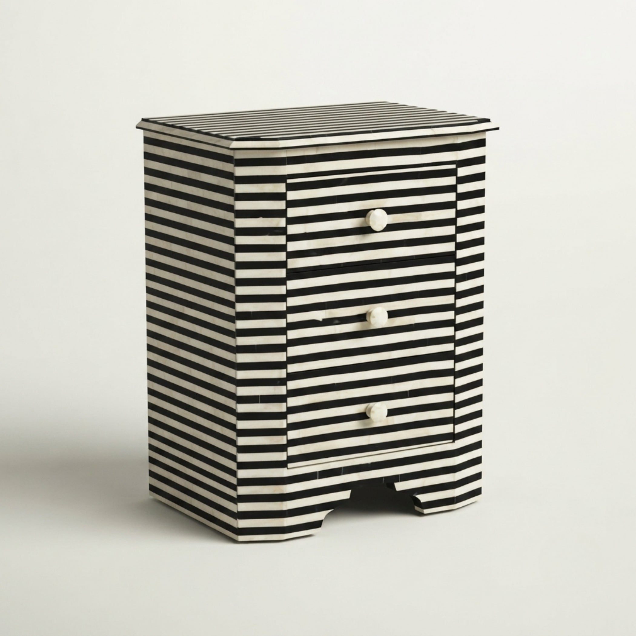 A small striped nightstand with three drawers, featuring a black and white horizontal pattern and three small white knobs, set against a plain light gray background.