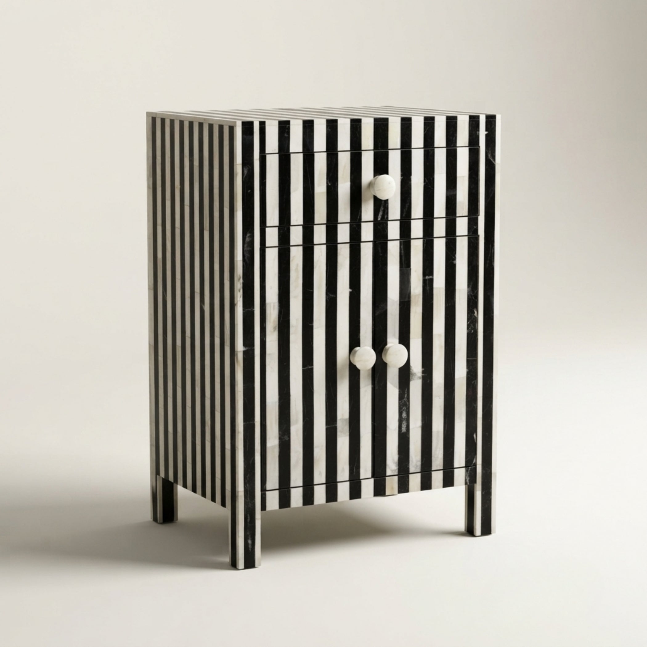 A small two-drawer nightstand with vertical black and white striped bone-inlay panels and two round white knobs, photographed on a clean light gray studio background.