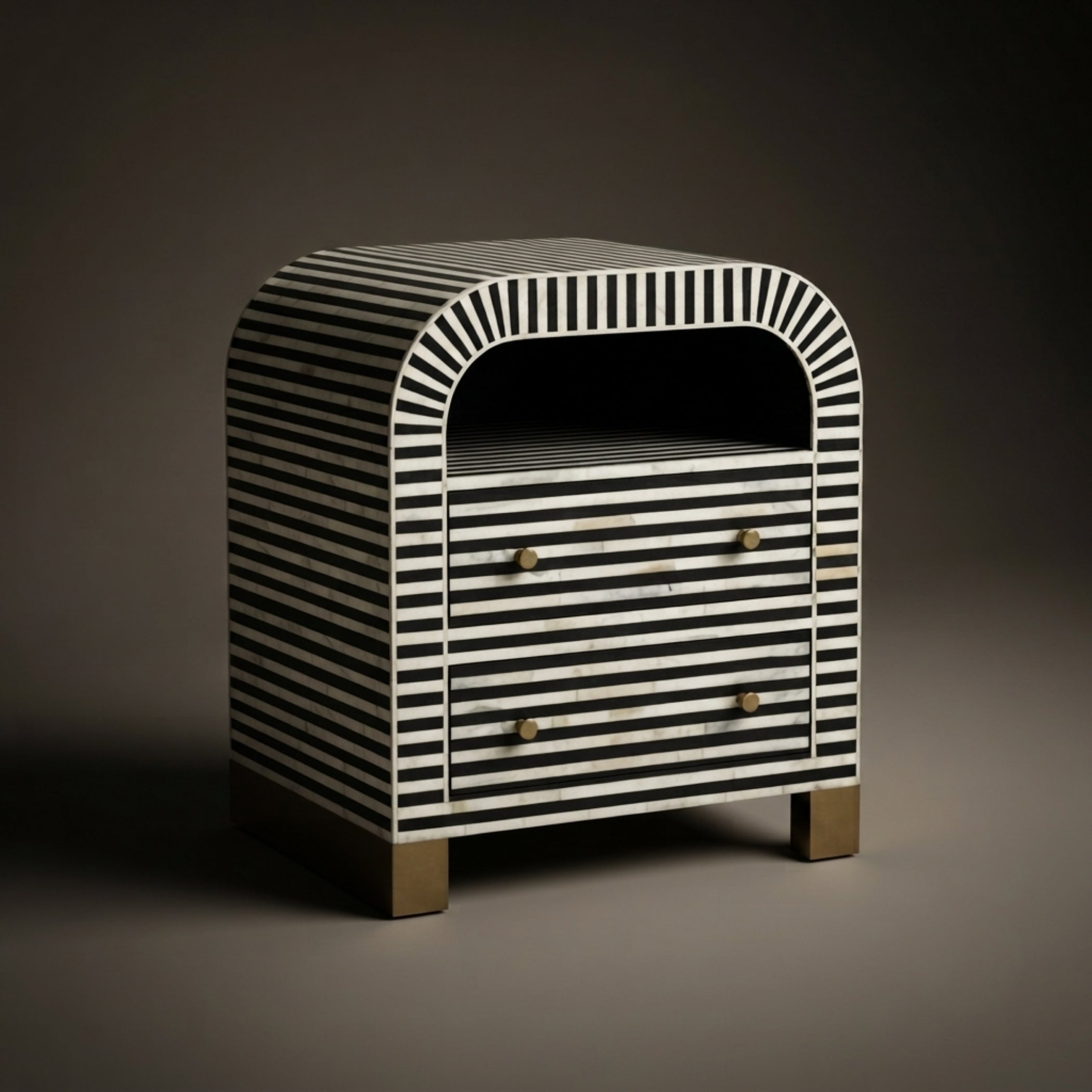 A modern side table or nightstand with a black and white striped bone-in-lay finish, featuring a rounded top, two drawers with brass knobs, and a small open shelf on top, set against a dark studio background.