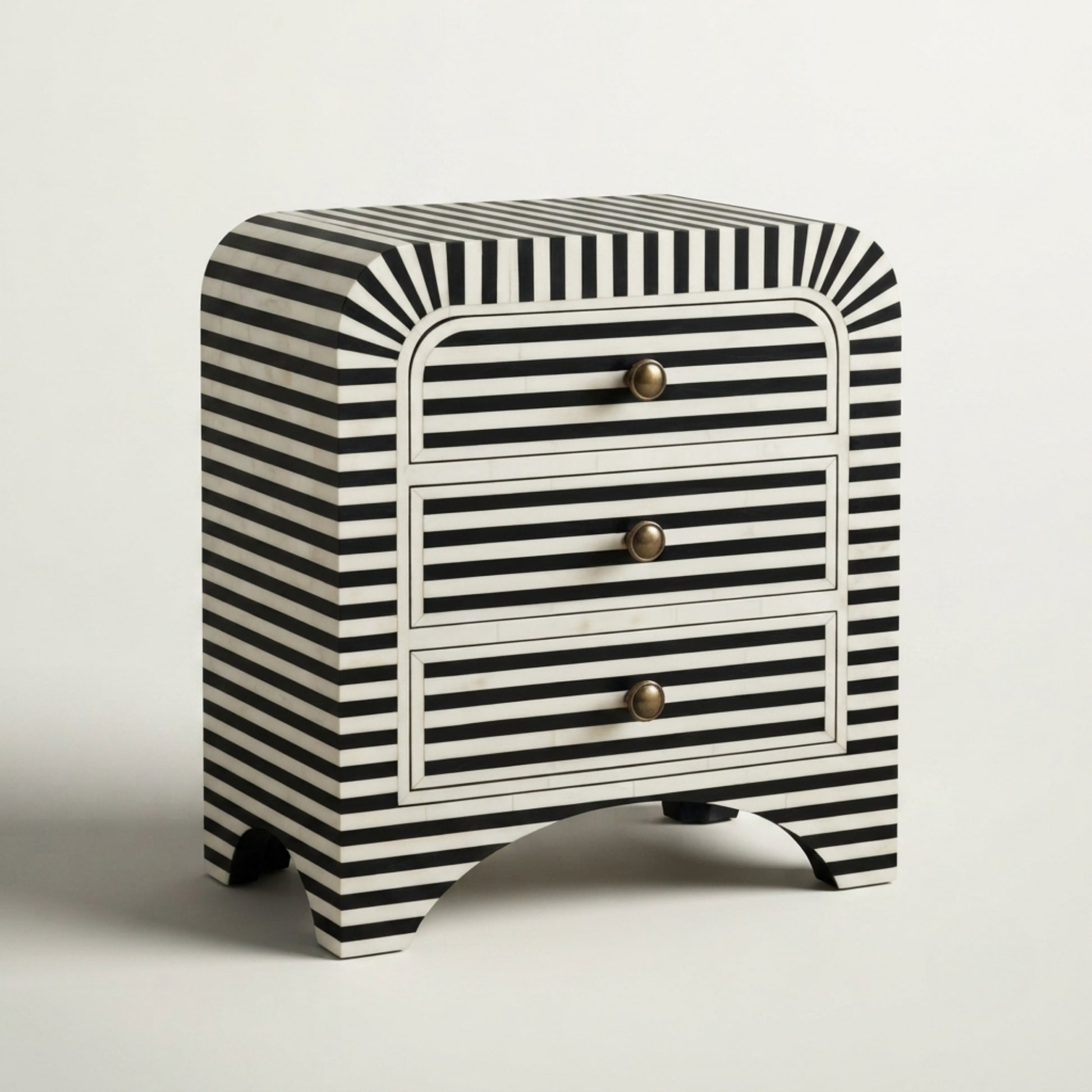 A small three-drawer nightstand with a bold black and white striped pattern, featuring curved legs and three brass pull knobs, set against a plain light gray background.