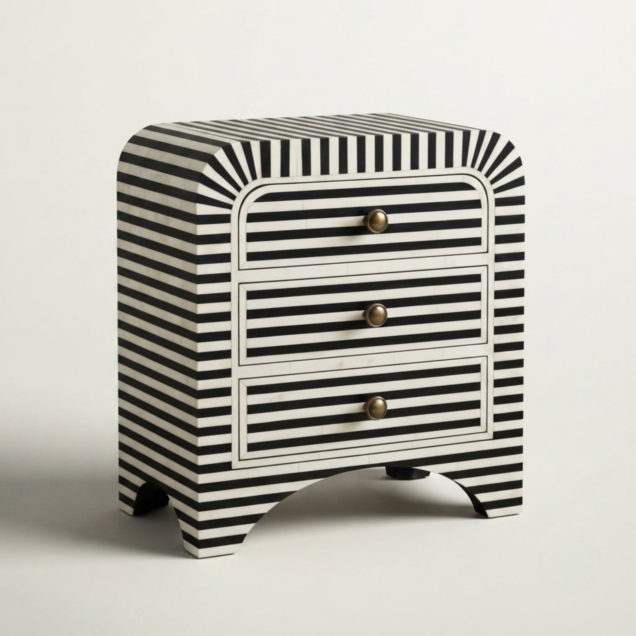 A small three-drawer nightstand with a bold black and white striped pattern, featuring curved legs and three brass pull knobs, set against a plain light gray background.