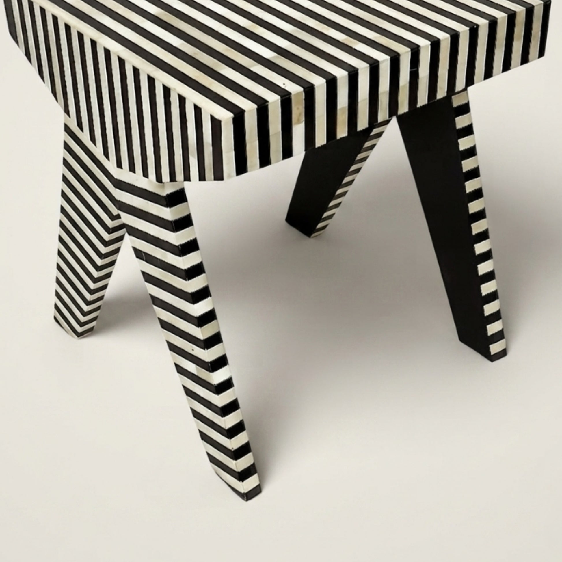 A modern bench or stool with a black and off-white striped bone-inwood style finish on the seat and legs, shown on a light gray studio background.