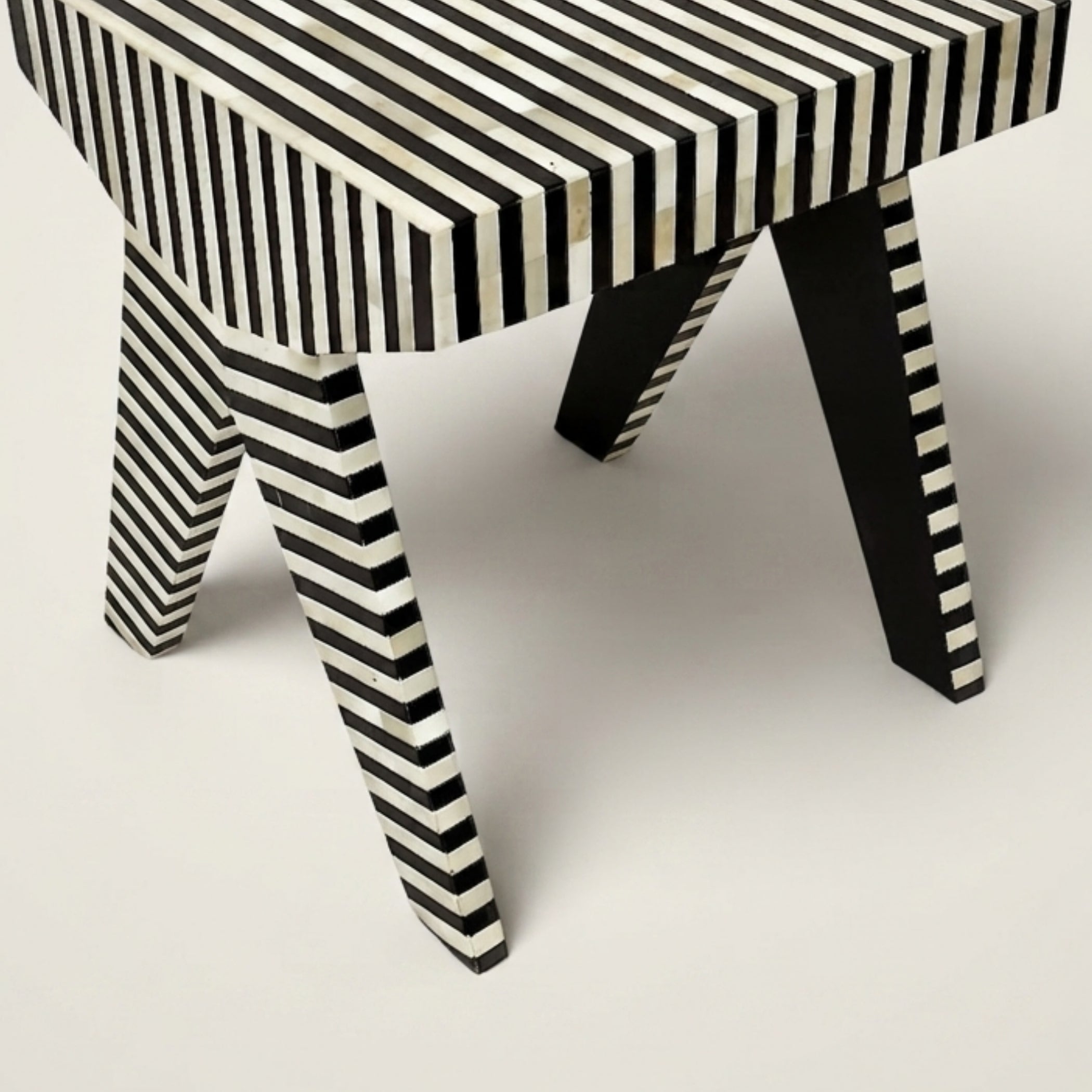A modern bench or stool with a black and off-white striped bone-inwood style finish on the seat and legs, shown on a light gray studio background.
