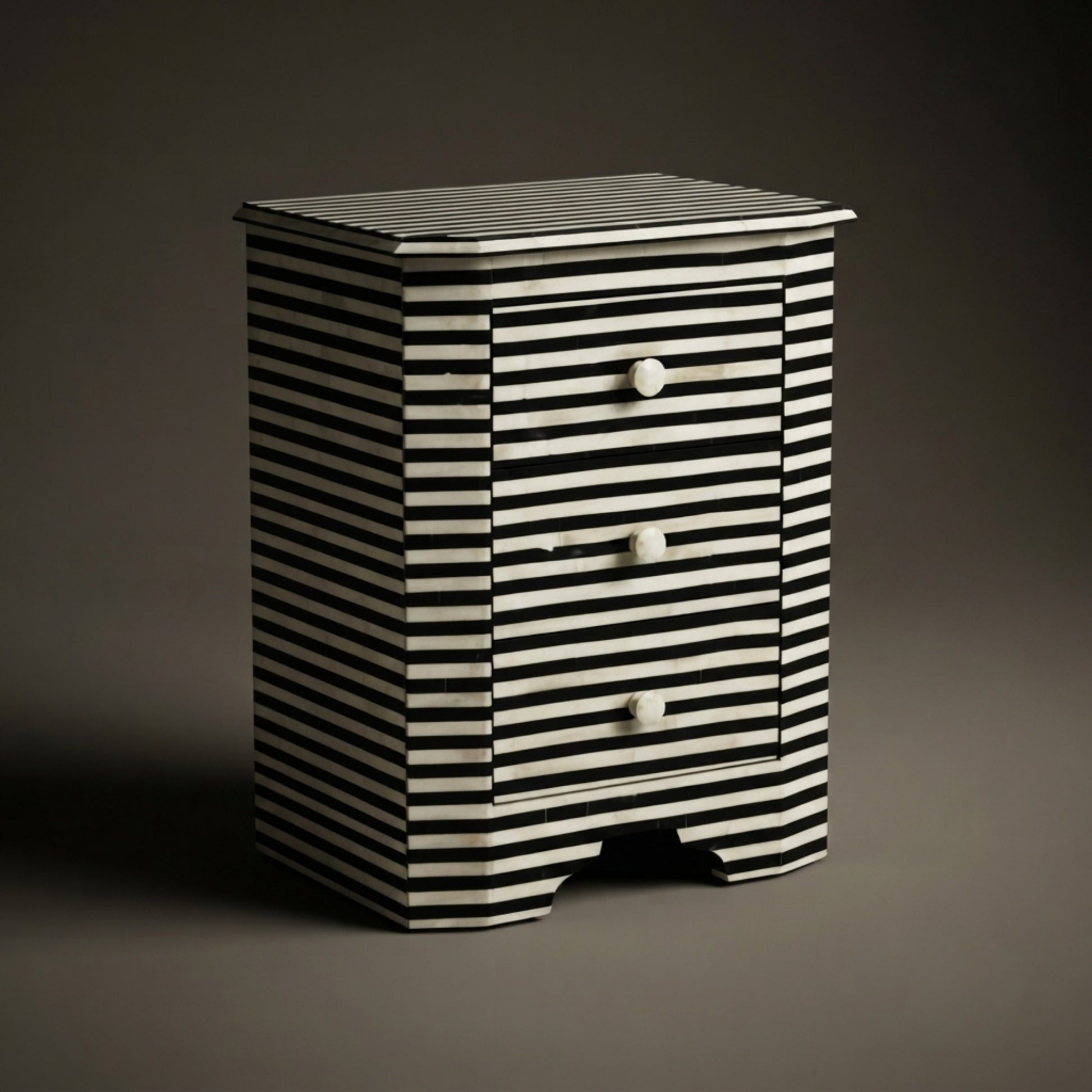 A small striped nightstand with three drawers and round white knobs, photographed against a dark gray studio background.