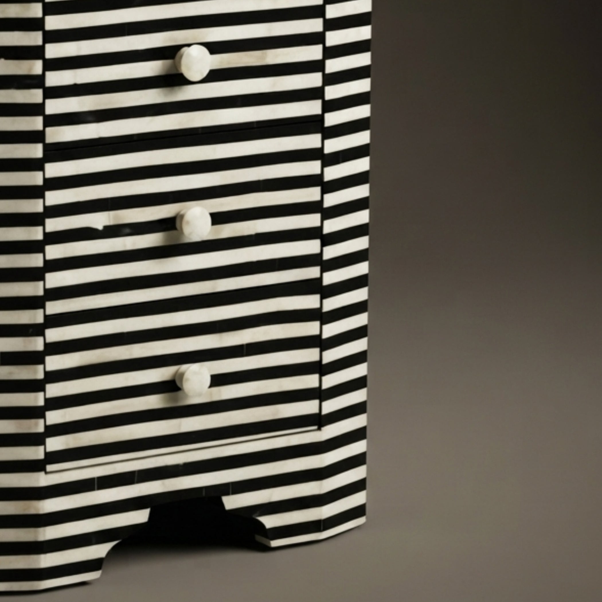 A close-up of a black and white striped wooden chest of drawers with three drawers and round white knobs, set against a dark gray background.