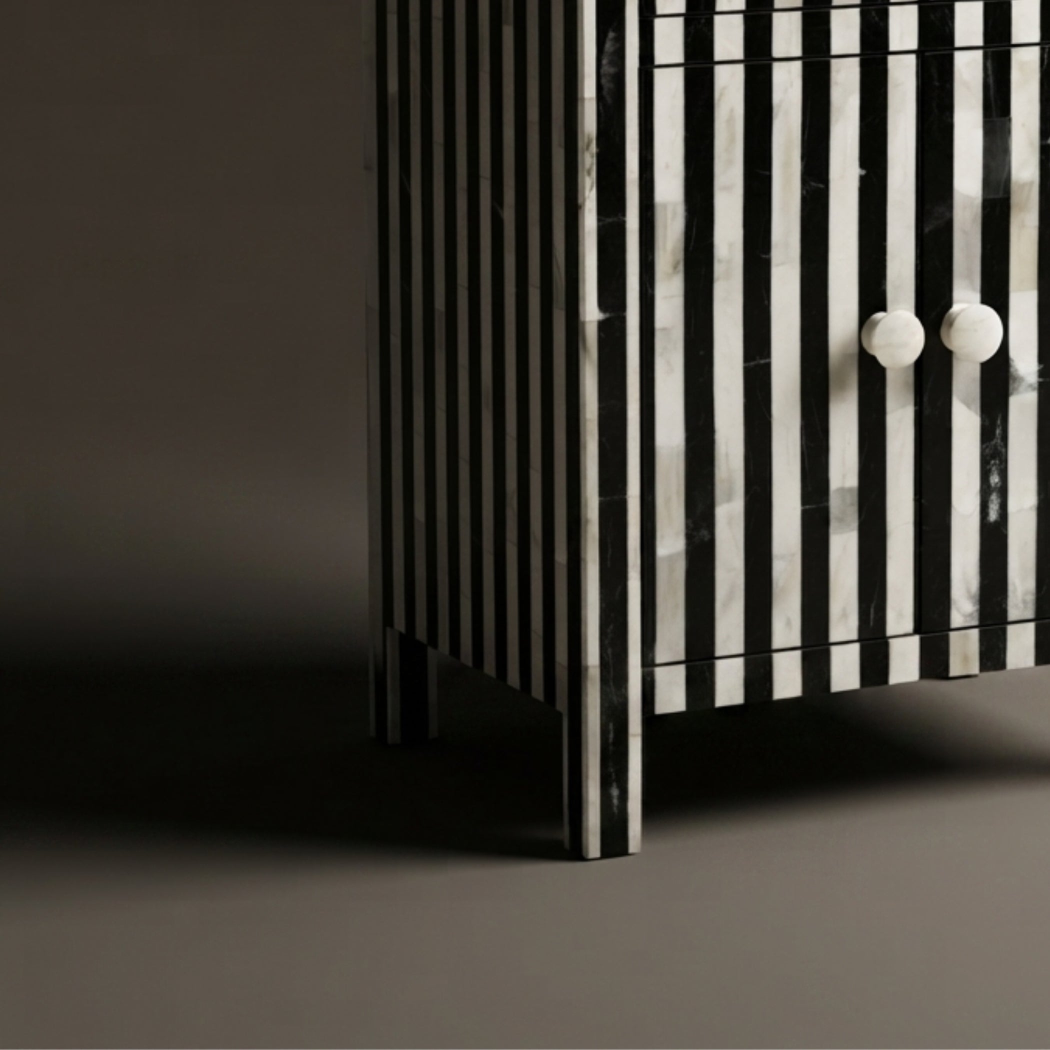 Close-up of a cabinet with vertical black and white striped bone-inlay panels and two round white knobs, photographed against a dark gray background.