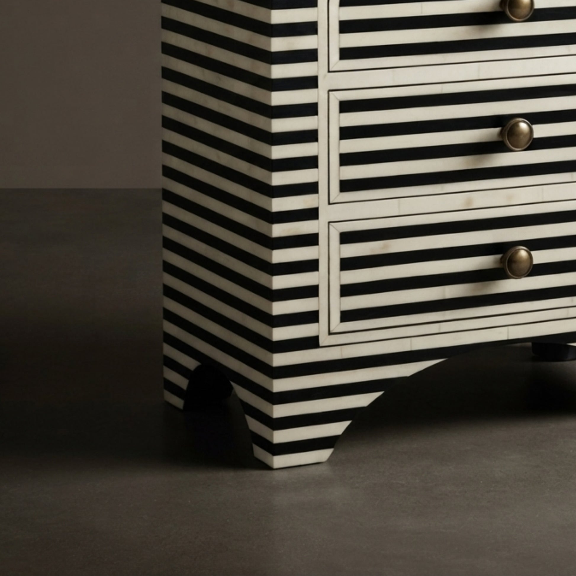 Close-up of a black and white striped wooden dresser with three drawers and round metallic knobs, set against a dark gray background.