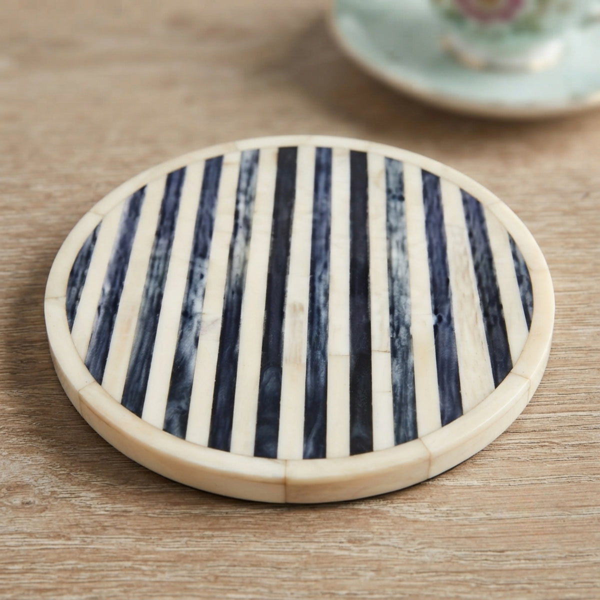 Round coasters with a striped pattern of dark navy and cream bone inlay, set on a wooden tabletop.