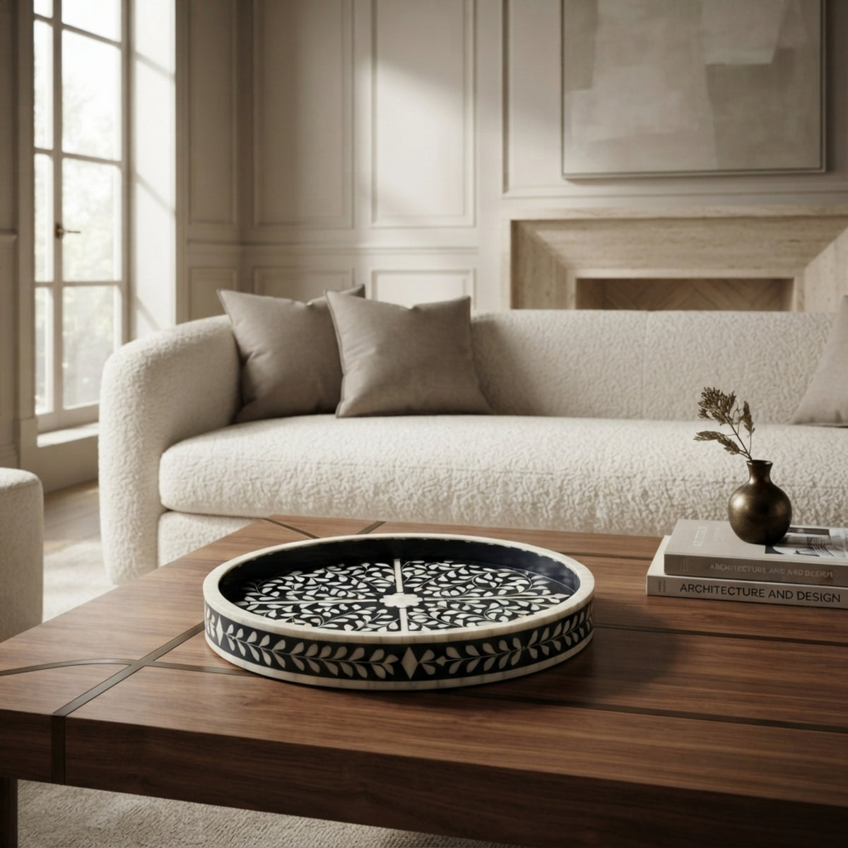 A round black and white patterned decorative tray sits on a dark wood coffee table in a modern living room setting with a textured cream boucle sofa in the background.