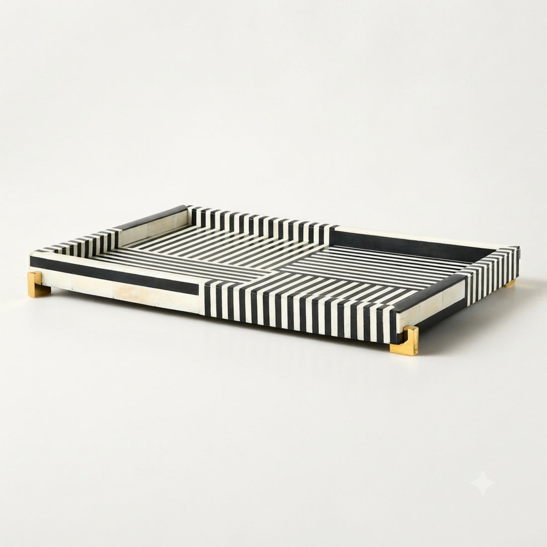 A rectangular serving tray with black and white striped bone-look sides and gold-toned feet, styled on a wooden coffee table in a modern living room setting.