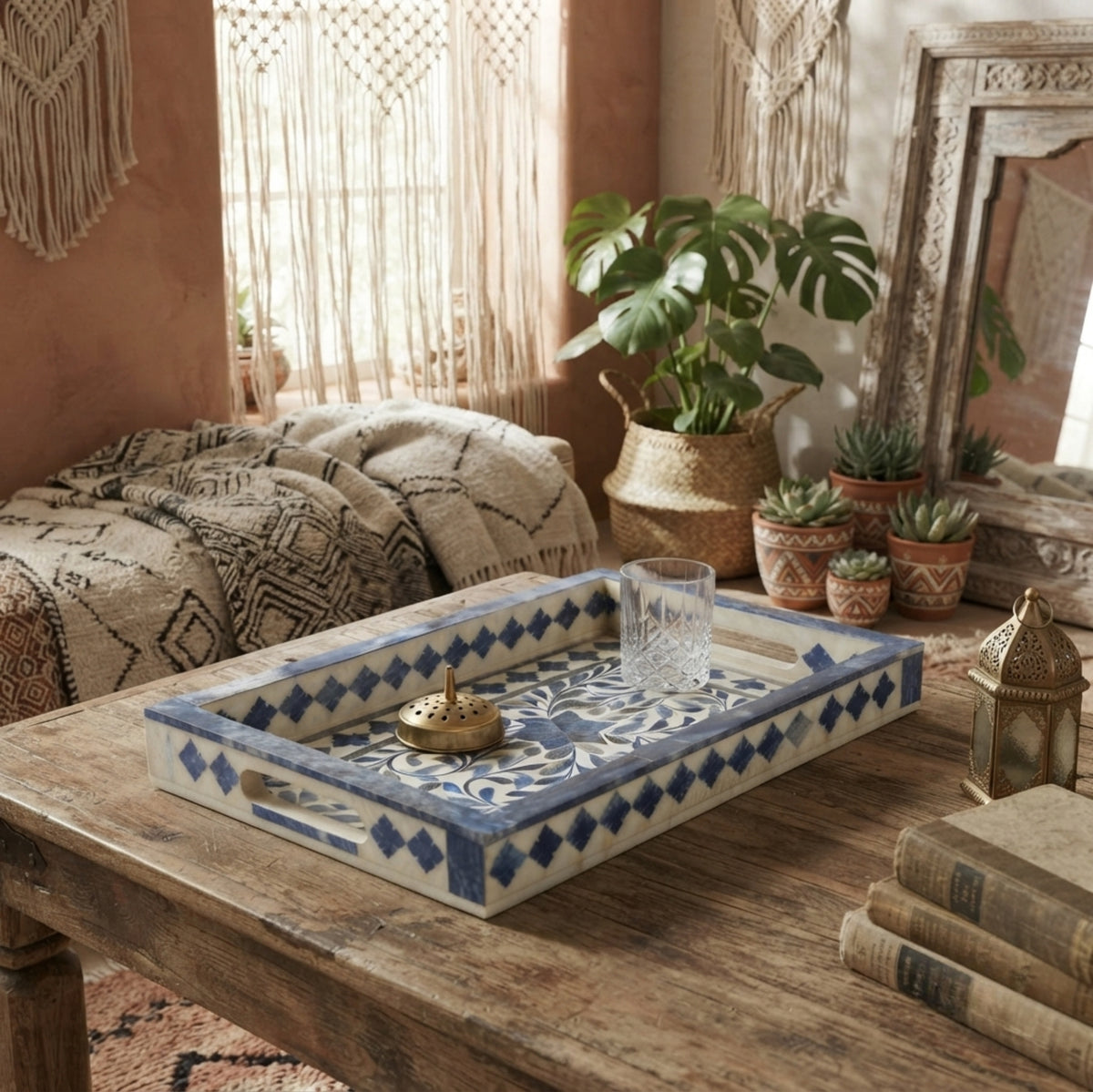 A rectangular decorative serving tray with blue and white bohemian-style tile patterns, styled on a rustic wooden coffee table in a warm, boho-living room setting.