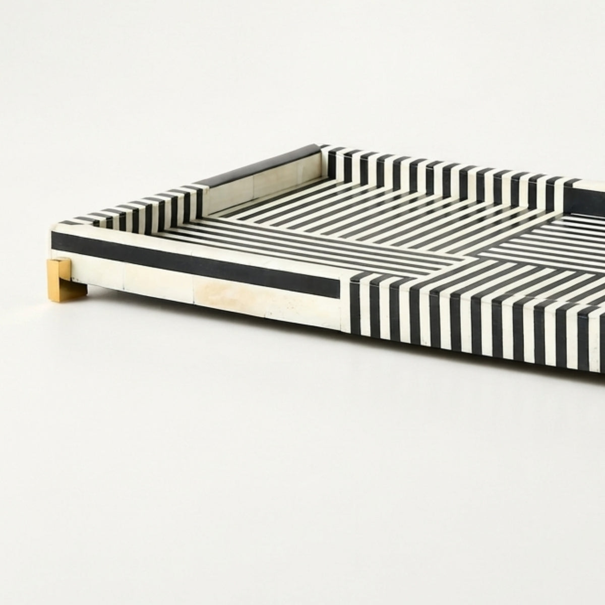 A rectangular serving tray with a black and white striped bone-in design and small gold metal feet, shown on a clean white background.