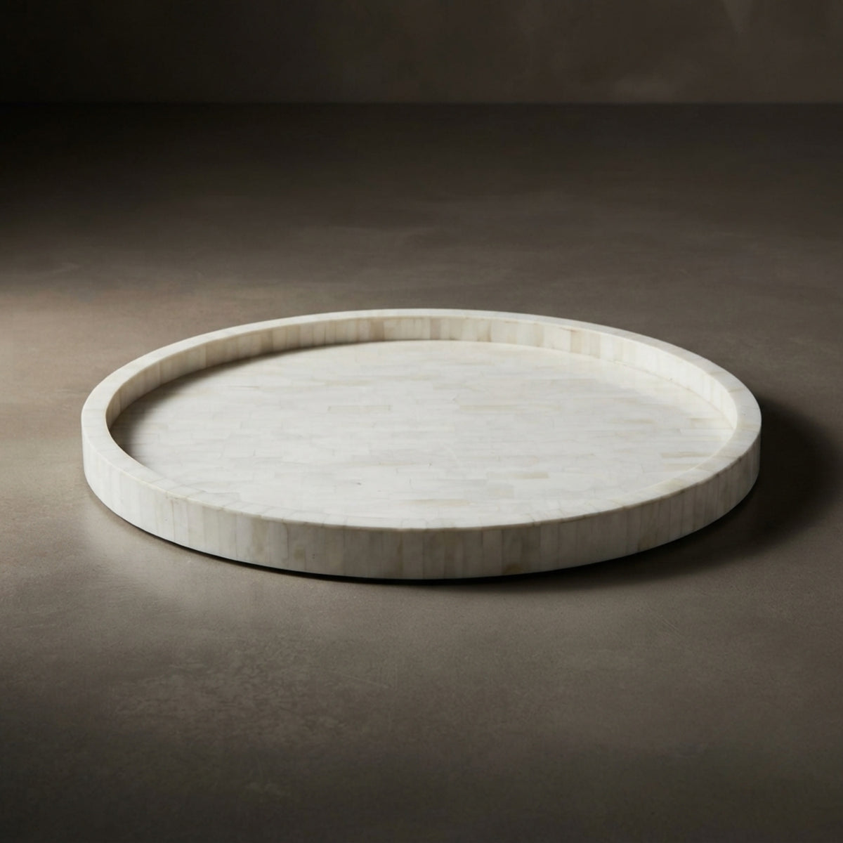 A round travertine stone serving tray with a natural organic border, photographed on a dark gray concrete surface.