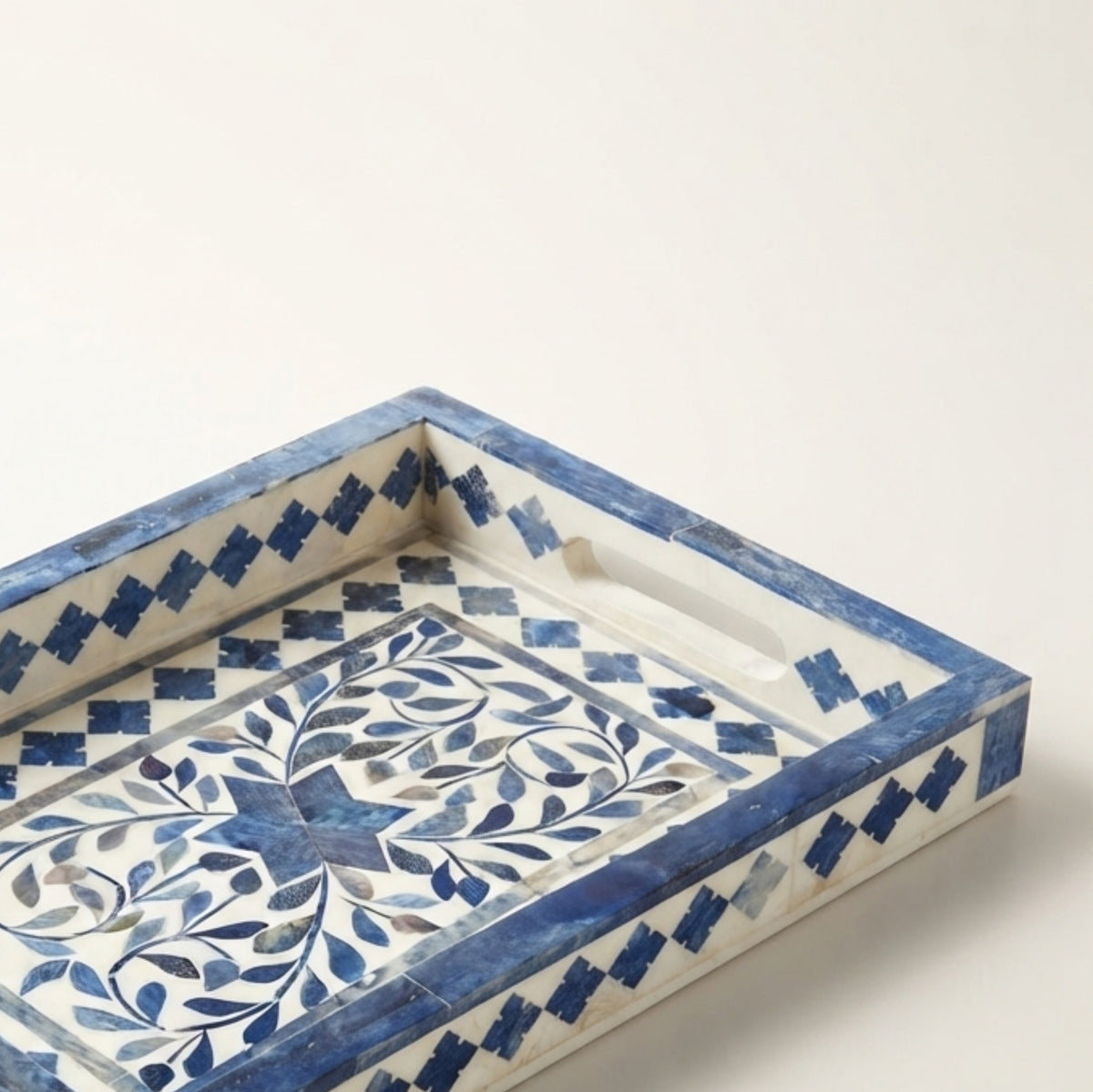 A rectangular decorative tray with a blue and white bone-in-wood inlay pattern, featuring a floral motif on the base and geometric borders, photographed on a light cream background.