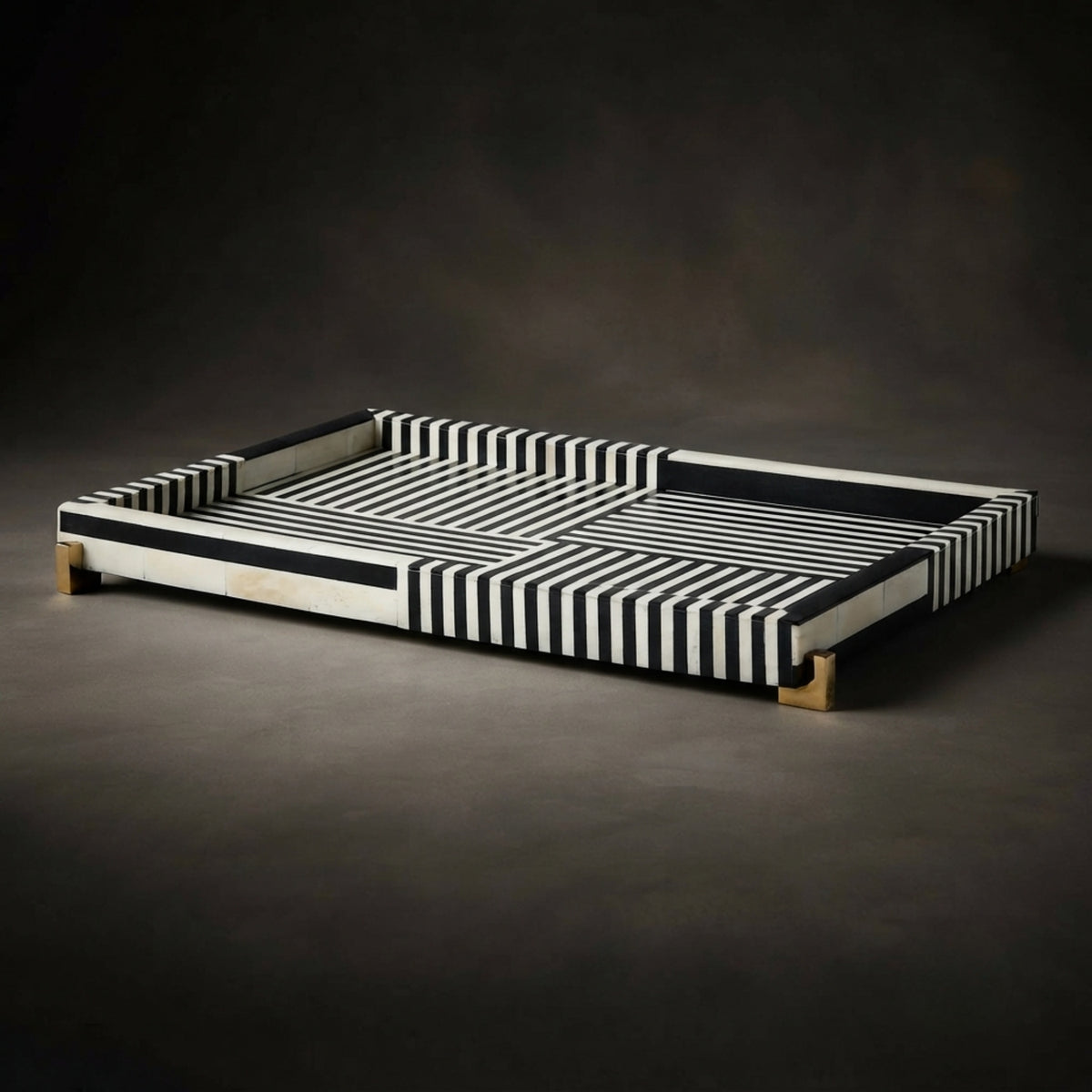 A rectangular tray with a black and white striped pattern and small natural wood feet, photographed on a dark studio background.
