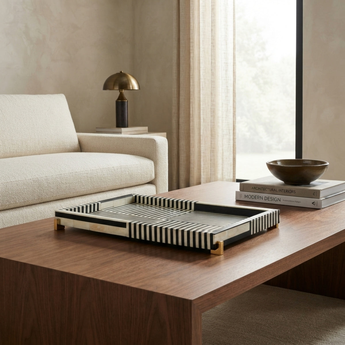 A rectangular serving tray with black and white striped bone-look panels and gold-toned legs, styled on a wooden coffee table in a modern living room setting.