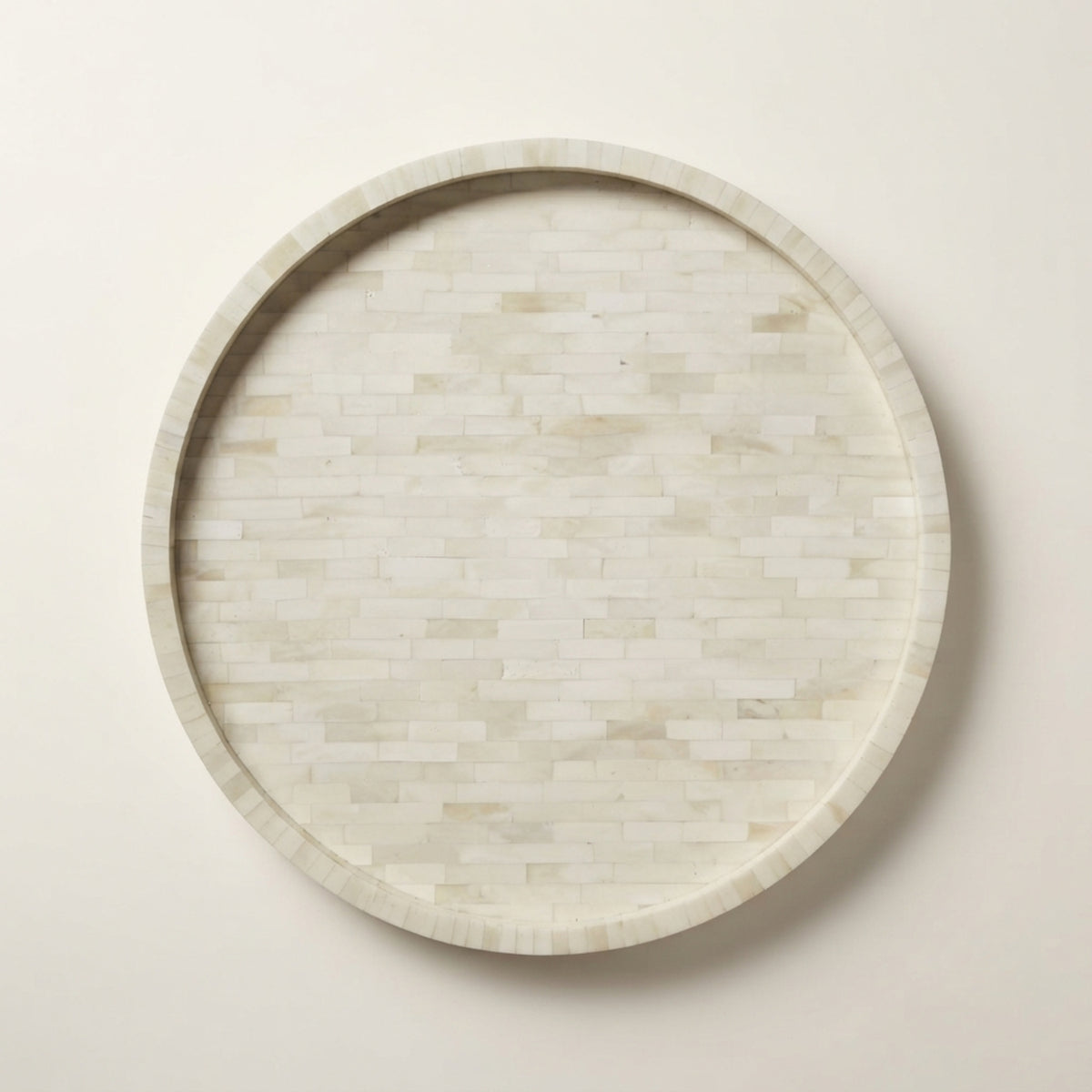 A round decorative tray with a light beige and white inlay pattern, photographed from directly above on a neutral cream background.