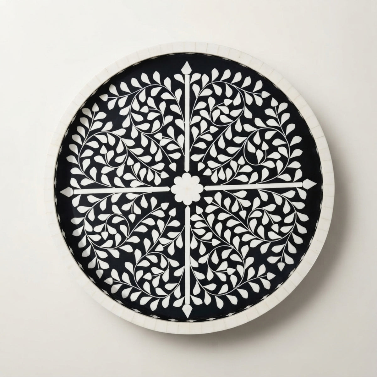 Round decorative wall plaque featuring a black and white botanical leaf pattern with a central floral motif, mounted on a light wall.
