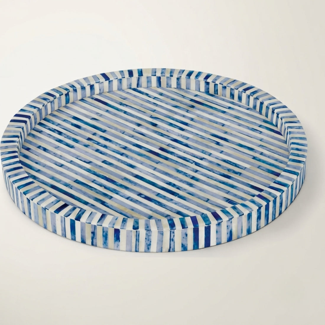 A round woven tray with blue and white stripes, filled with fruit, placed on a wooden coffee table in a bright, modern living room.