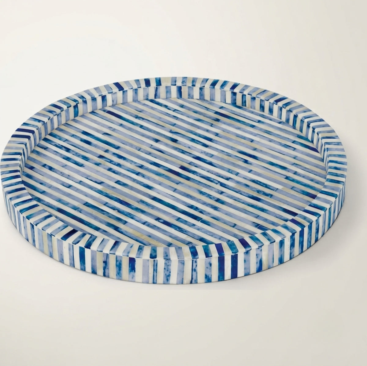 Round decorative tray with a striped pattern in shades of blue, navy, and white, shown from a top-down angle on a light beige background.