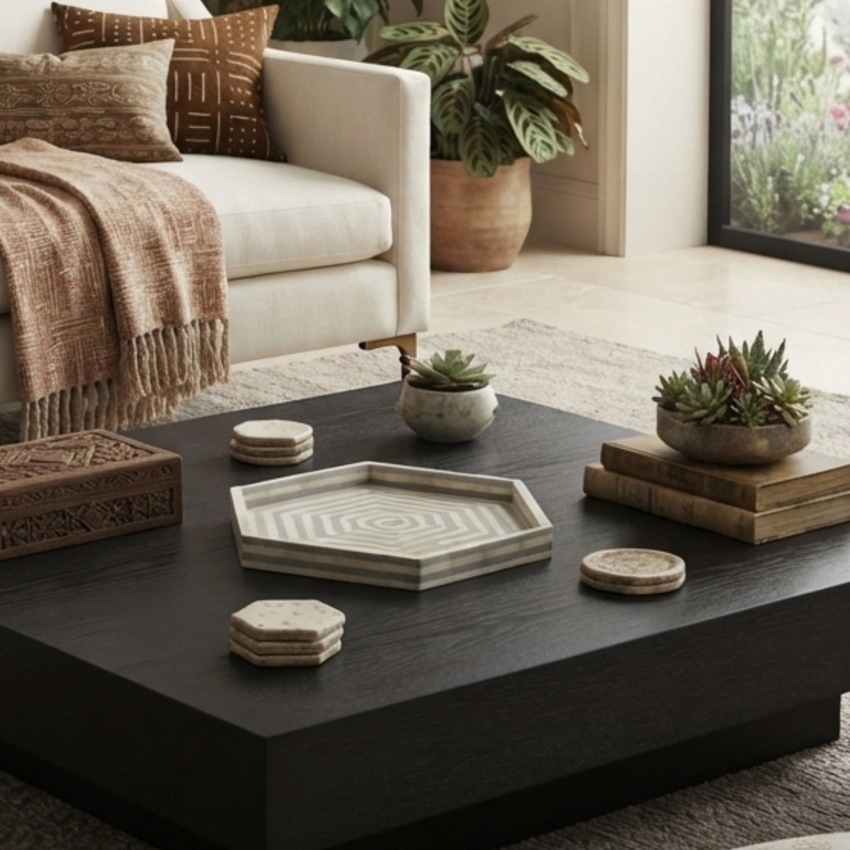 A modern dark wood coffee table in a styled living room, decorated with a hexagonal tray, coasters, books, and small potted succulents.