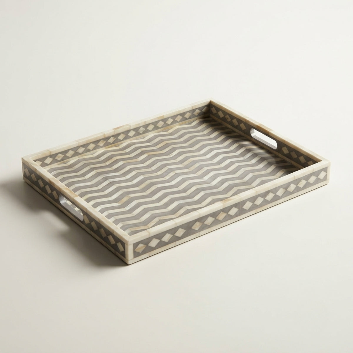 A rectangular serving tray with cutout handles, featuring a gray and white wavy chevron pattern on the bottom and beige inlay borders with small diamond motifs, shown on a light gray background.