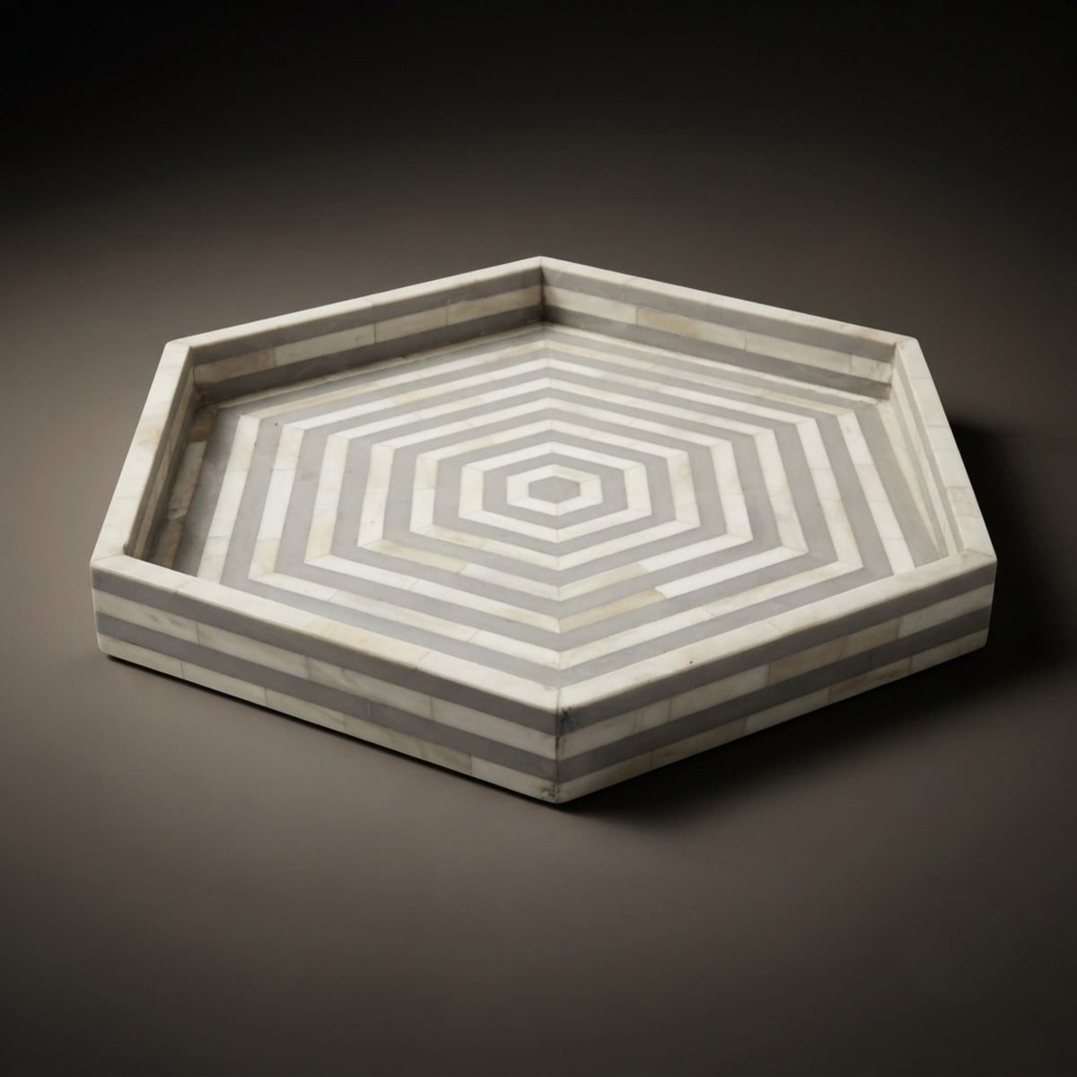 Hexagonal decorative tray made of light gray and white striped bone inlay, photographed on a dark gray gradient background.