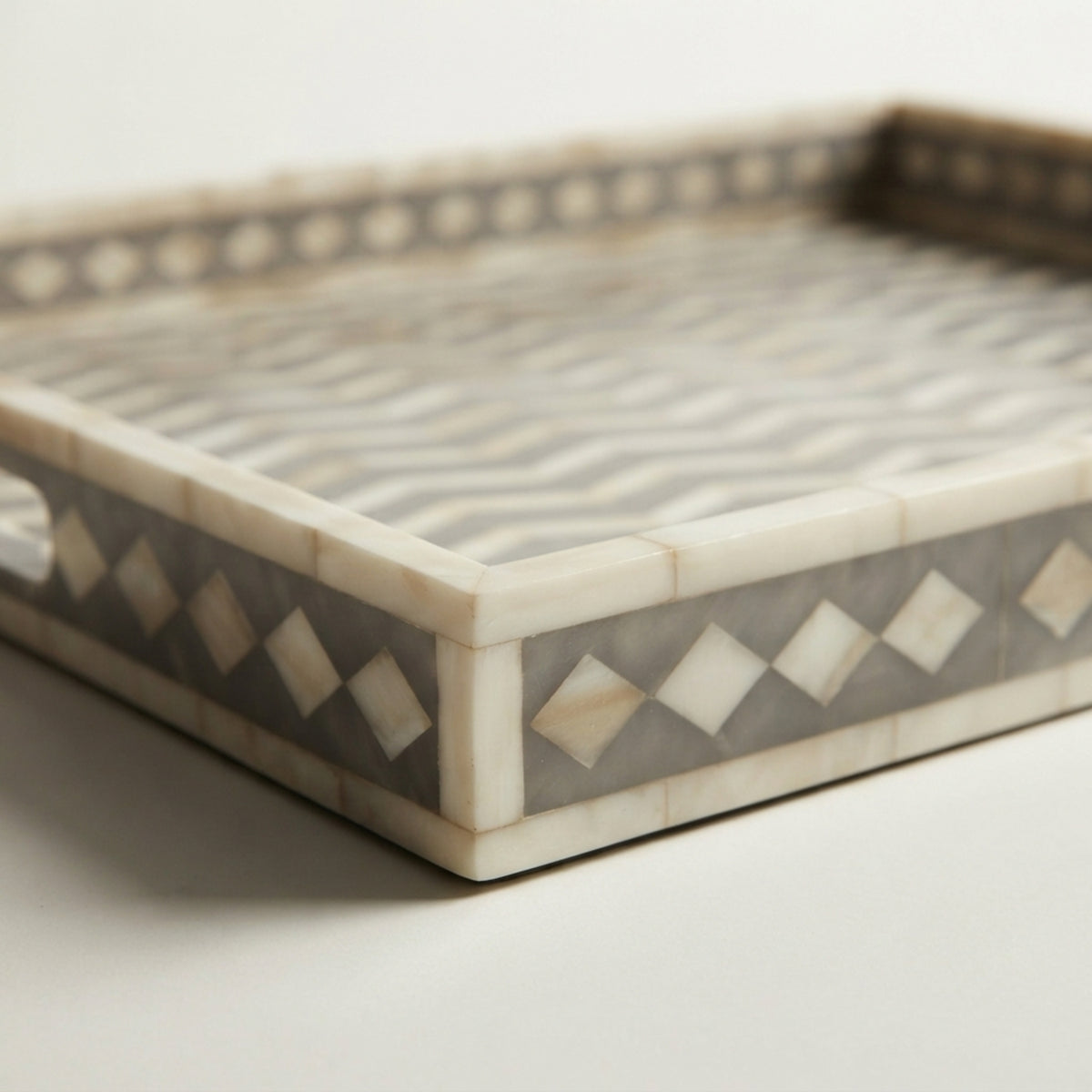 A rectangular decorative tray with an inlay design featuring wavy gray and white stripes on the top surface and diamond patterns on the sides, set against a plain light background.