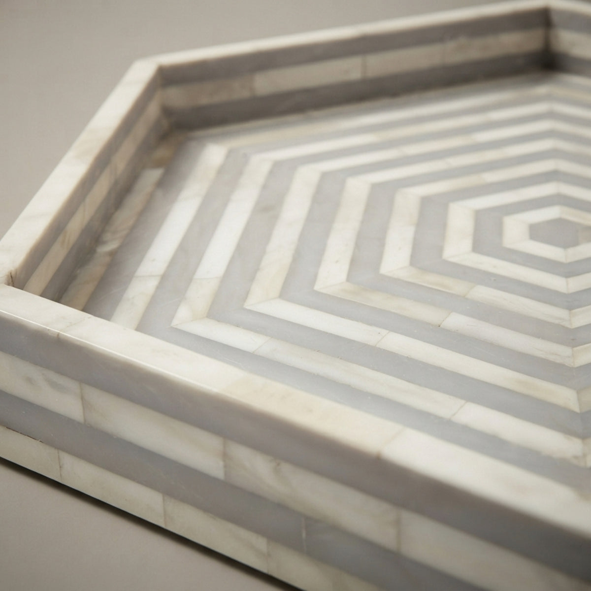A close-up of a hexagonal marble tray with concentric geometric patterns in white and gray.