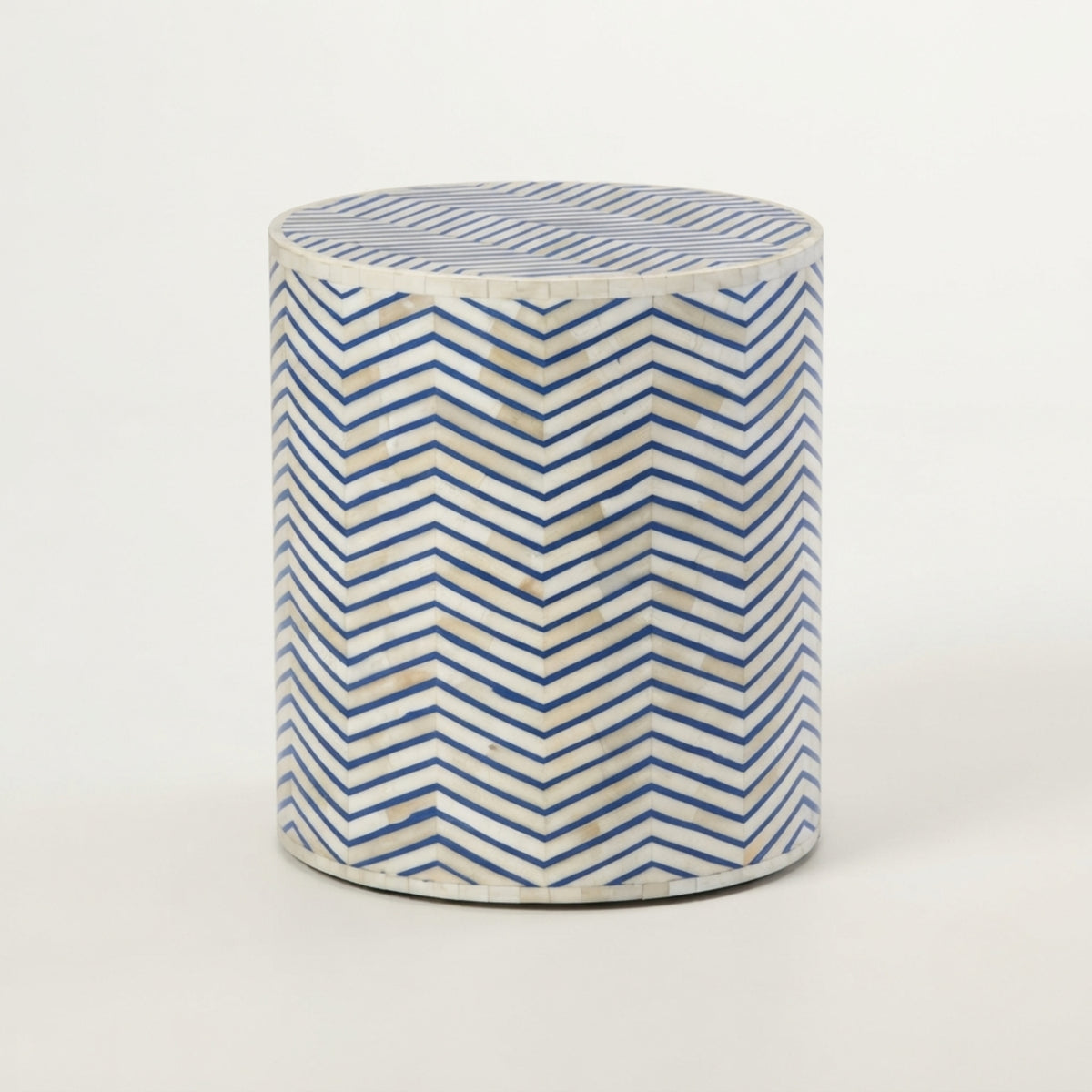 A cylindrical side table or stool with a blue and white chevron pattern inlaid on a light background, photographed against a plain white studio backdrop.