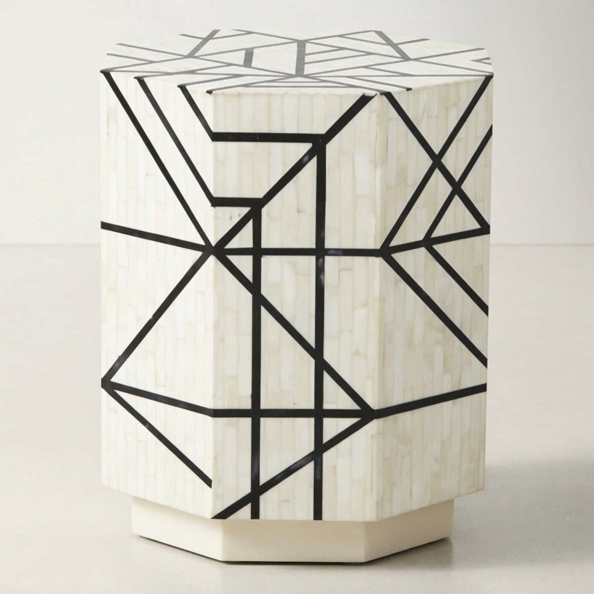 A hexagonal side table with a white bone inlay shell finish and a black geometric line pattern, set against a plain light background.