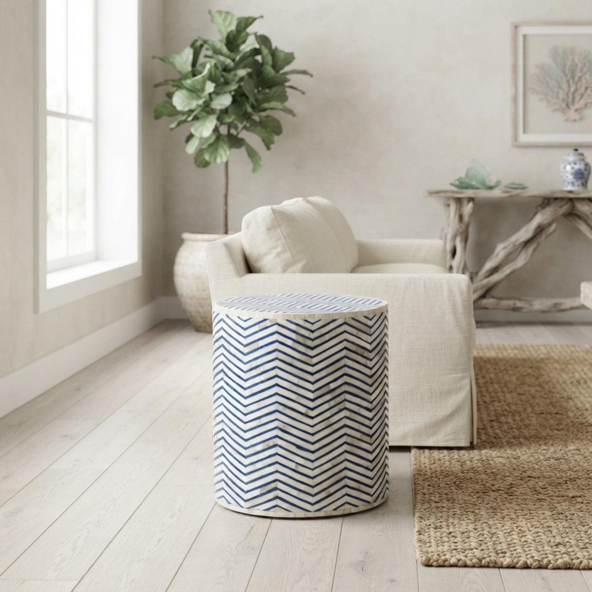 A cylindrical side table with a navy blue and white chevron pattern, styled in a bright, modern living room next to a cream-colored armchair and a woven rug.