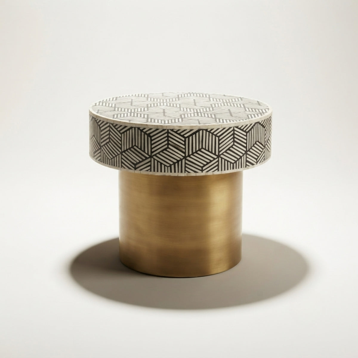A modern cylindrical side table featuring a brushed brass gold base and a round top with a black and white geometric cube pattern, set against a clean white background.