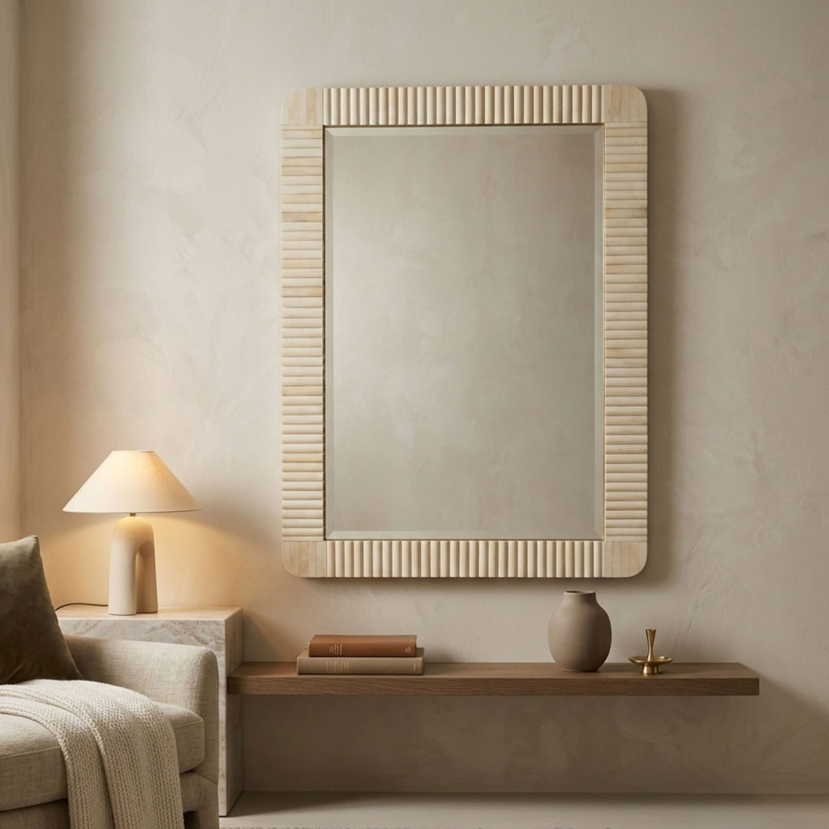 A large rectangular wall mirror with a ribbed natural wood frame hangs on a textured beige wall above a floating wooden shelf in a styled living room setting.