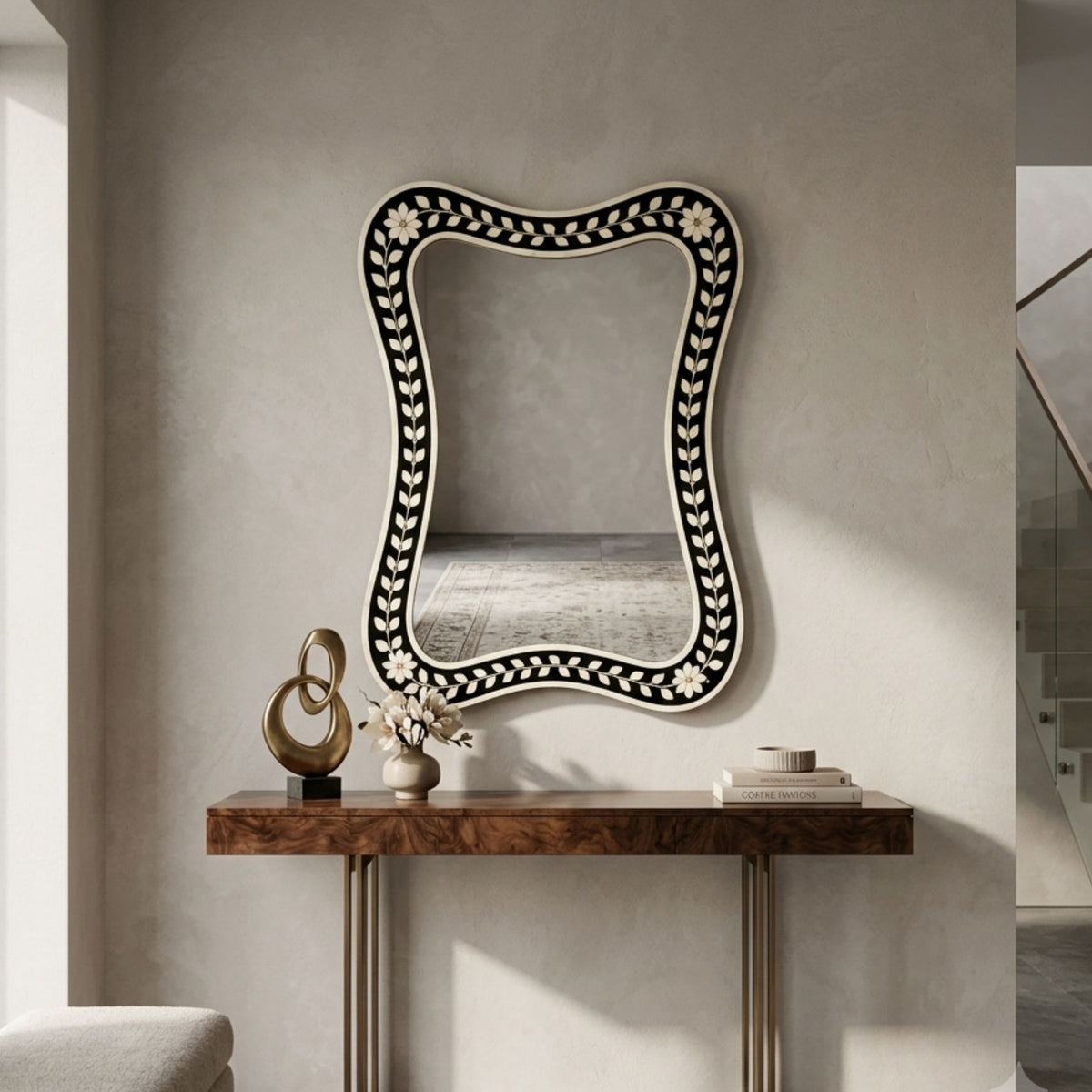 A decorative wall mirror with a black and white floral border, mounted on a textured beige wall above a wooden console table with decorative objects.