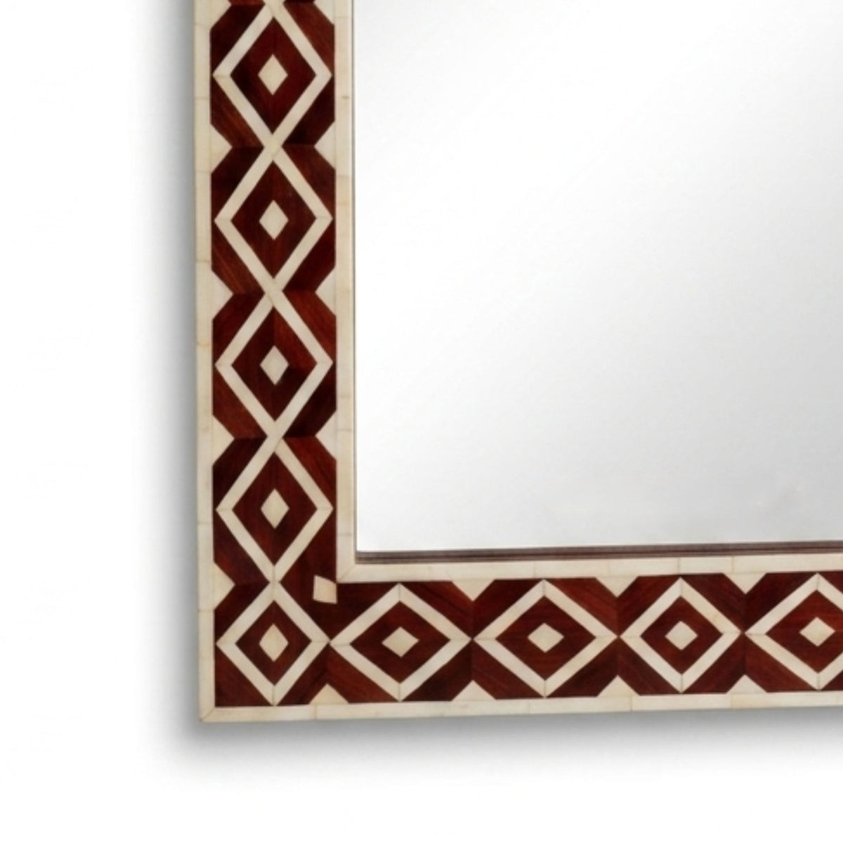 A close-up of a decorative rectangular mirror showing part of its frame, featuring a geometric diamond pattern in dark red and cream on a white background.