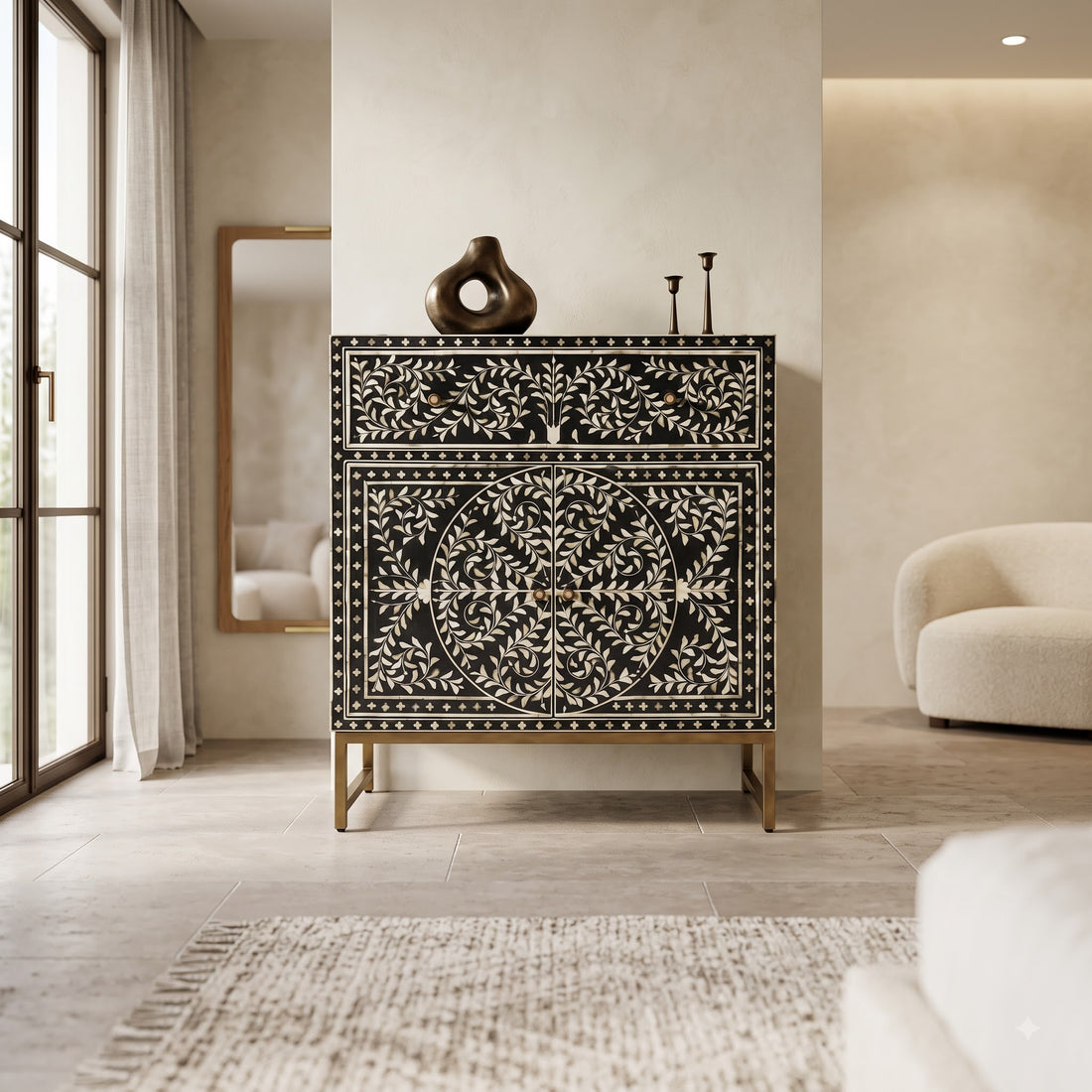 A black and white bone-inset chest of drawers with gold legs, styled in a modern, warm-toned living room next to a window and a curved cream sofa.