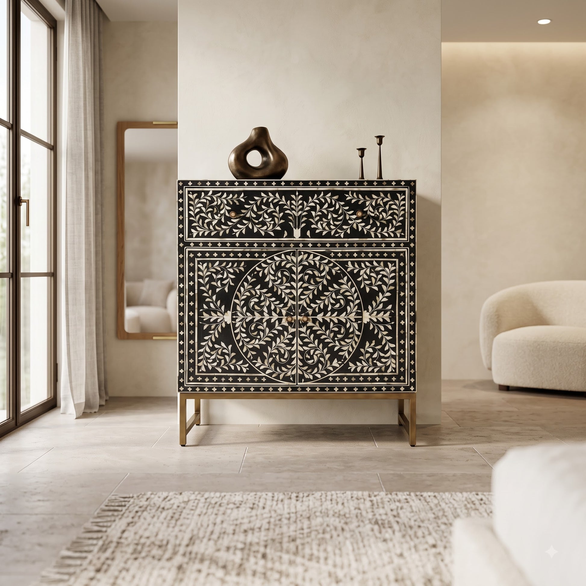 A black and white bone-inset chest of drawers with gold legs, styled in a modern, warm-toned living room next to a window and a curved cream sofa.