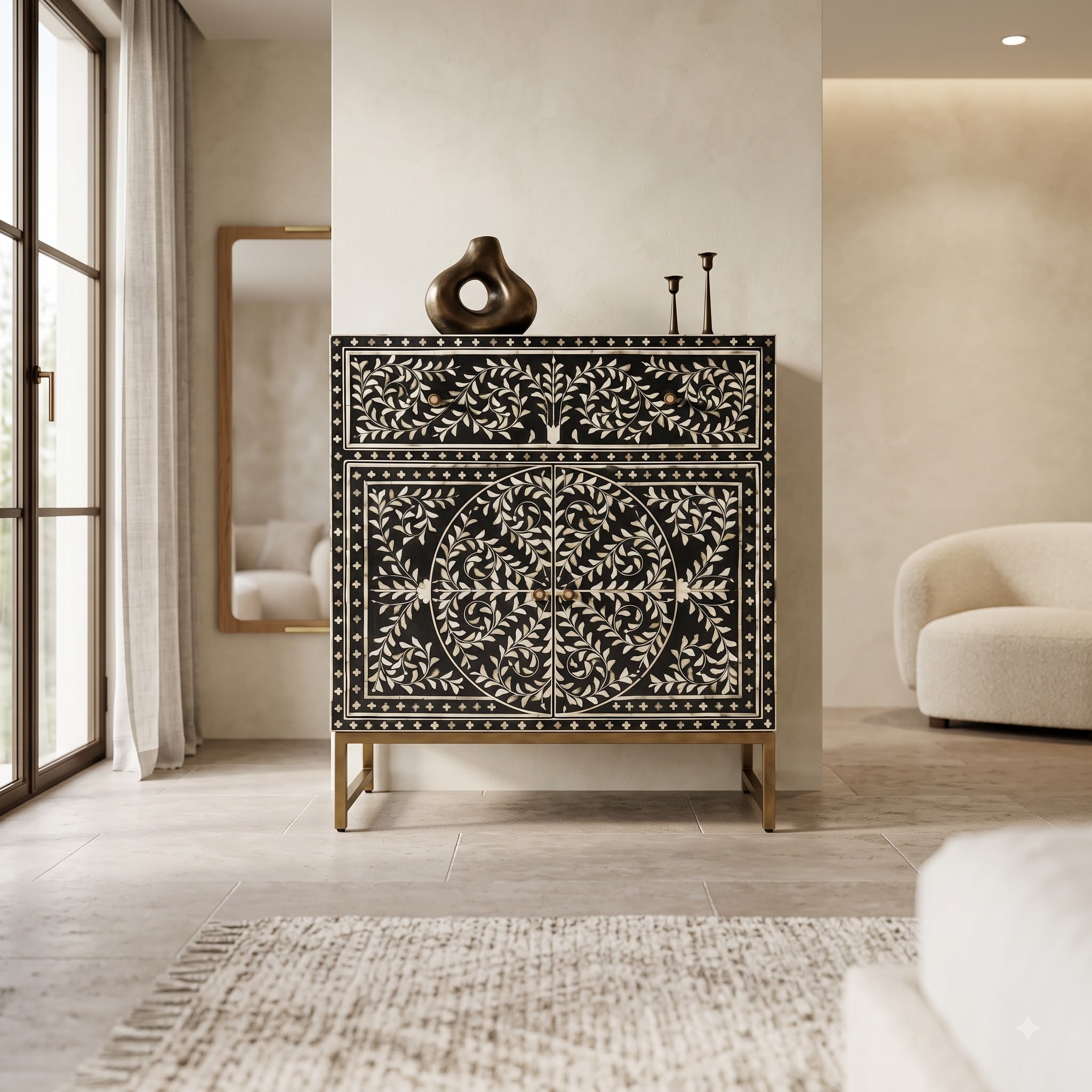 A black and white bone-inset chest of drawers with gold legs, styled in a modern, warm-toned living room next to a window and a curved cream sofa.