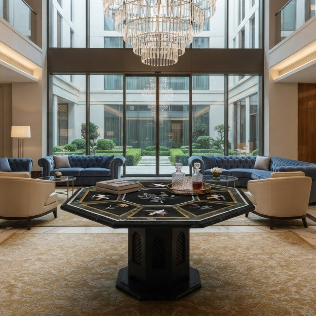 Handmade black marble octagonal table top with colorful bird pietra dura inlay displayed in a luxury hotel lobby with modern seating and crystal chandelier.