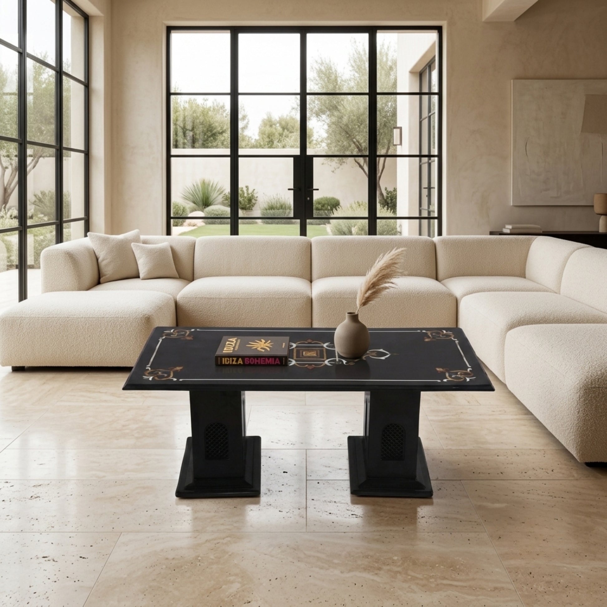 A modern living room featuring a large cream-colored sectional sofa and a black rectangular coffee table with gold decorative borders. The room has beige walls, large black-framed windows, and a light stone tile floor.