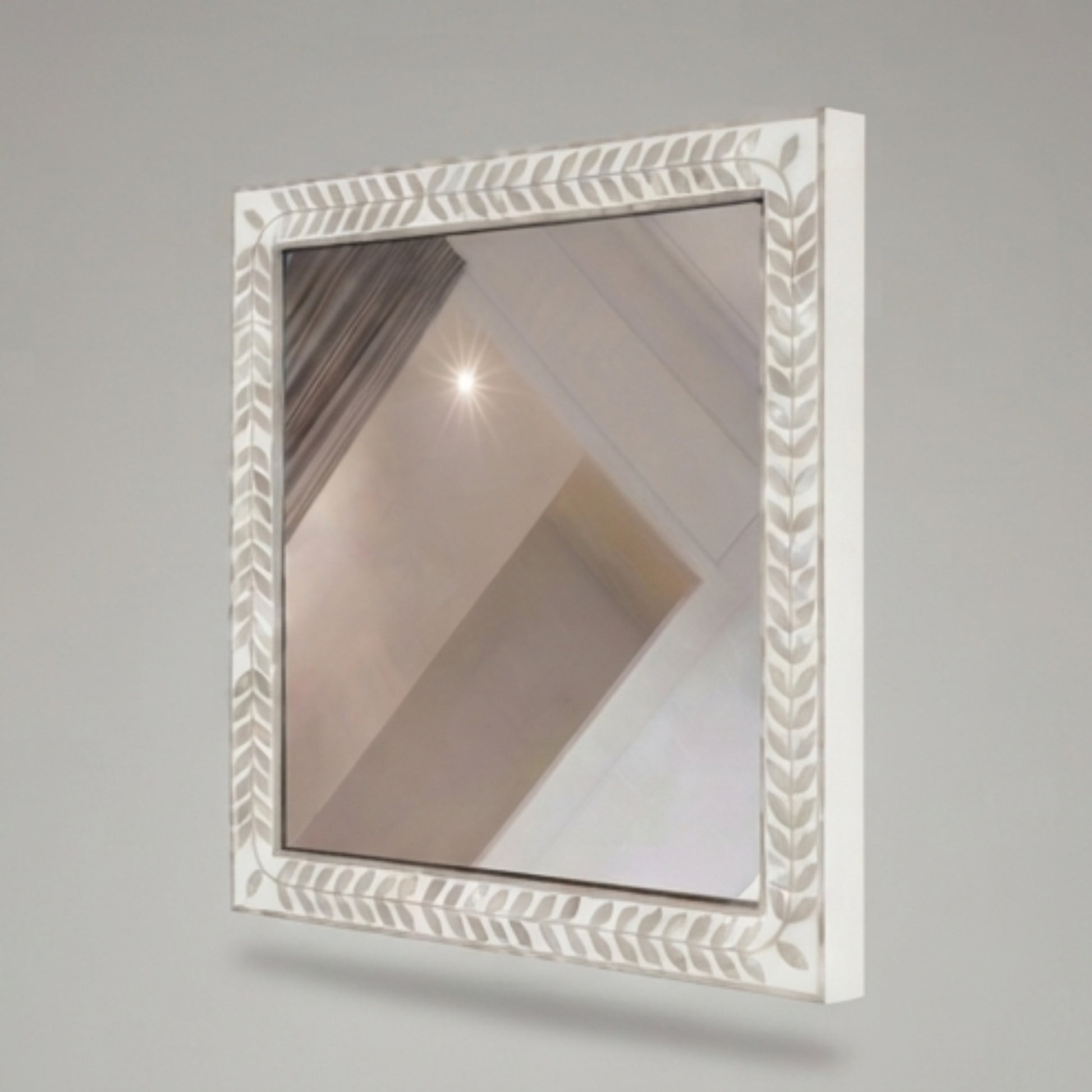A square wall mirror with a white carved frame featuring a leaf or feather pattern, shown against a neutral gray background.