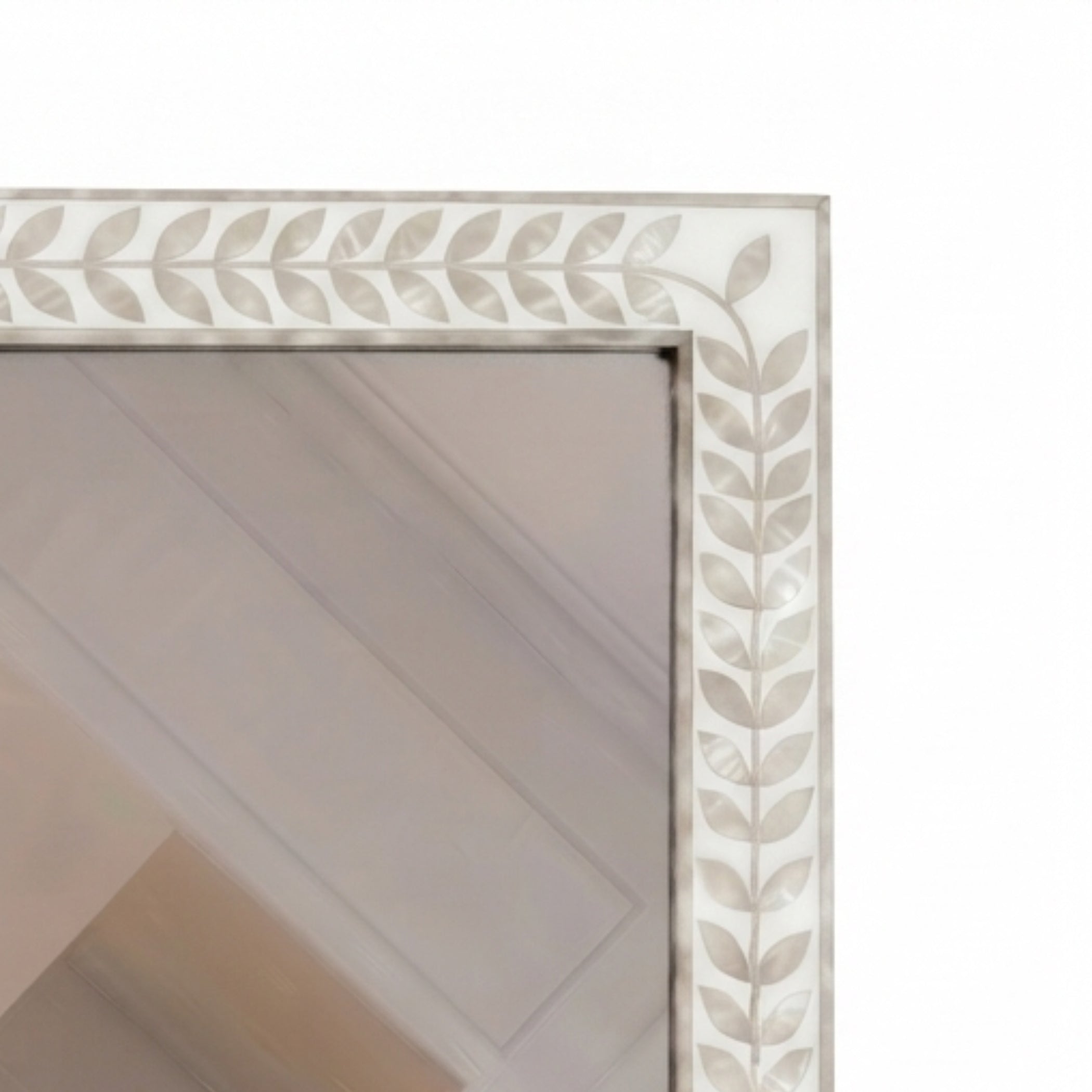 Close-up of a rectangular mirror with an ornate white and beige leaf-patterned frame, showing a reflection of a paneled ceiling.