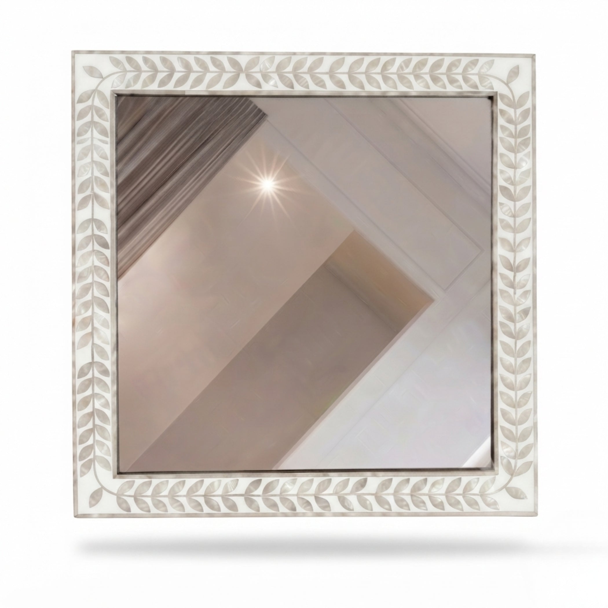 A square decorative mirror with an ornate white leaf-patterned frame, reflecting a neutral-toned interior ceiling and walls.