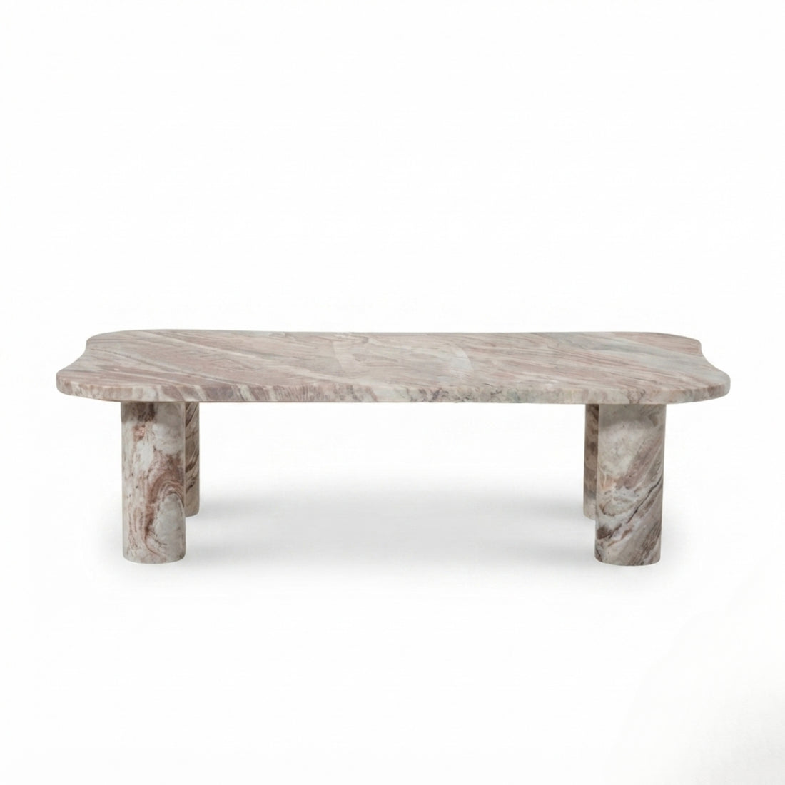 A rectangular coffee table with a polished pinkish-beige marble top and carved stone legs, styled in a warm living room next to a beige sofa on a woven rug.