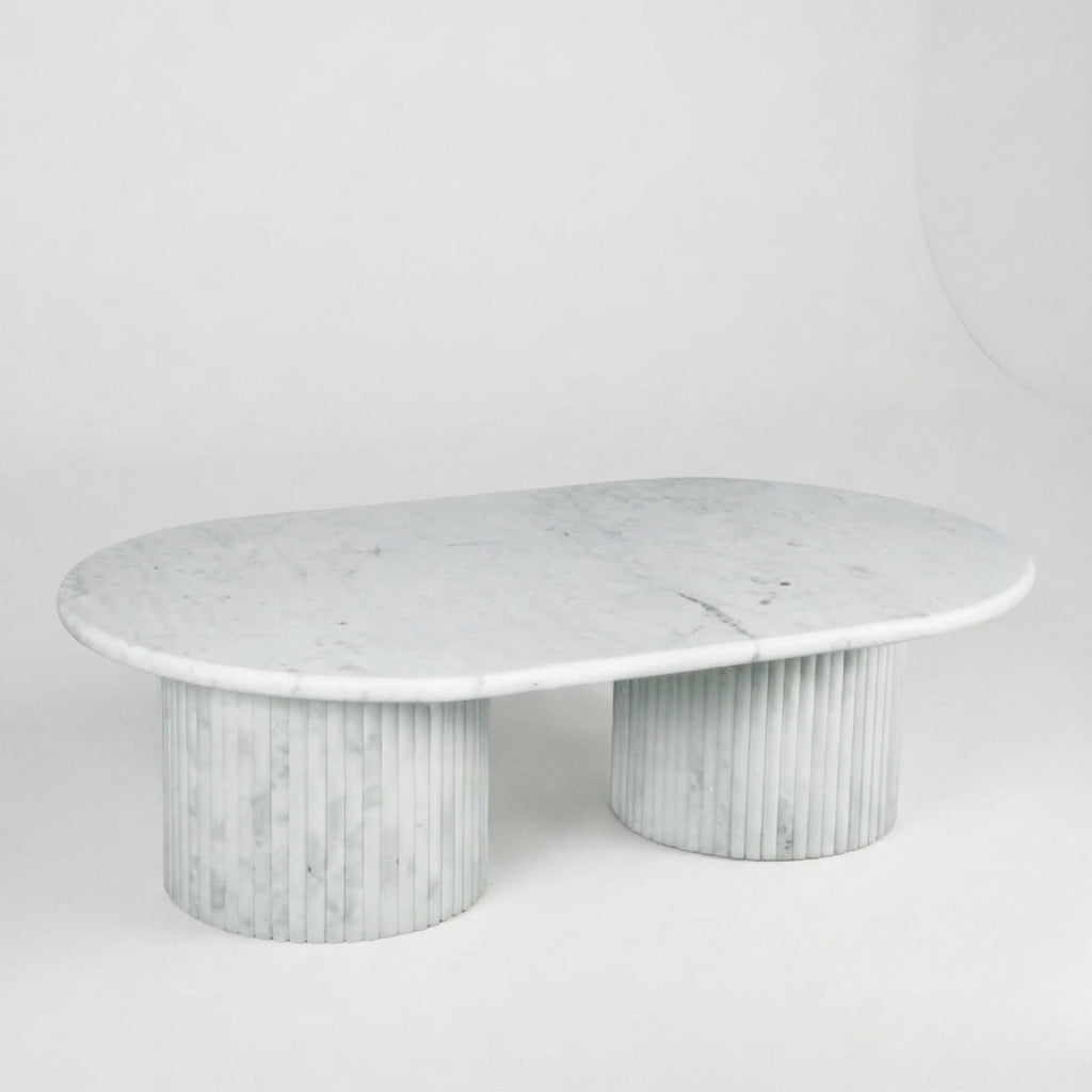 A modern oval coffee table made of white marble with subtle gray veining, featuring a smooth top and two fluted cylindrical pedestal bases, set against a seamless light gray studio background.