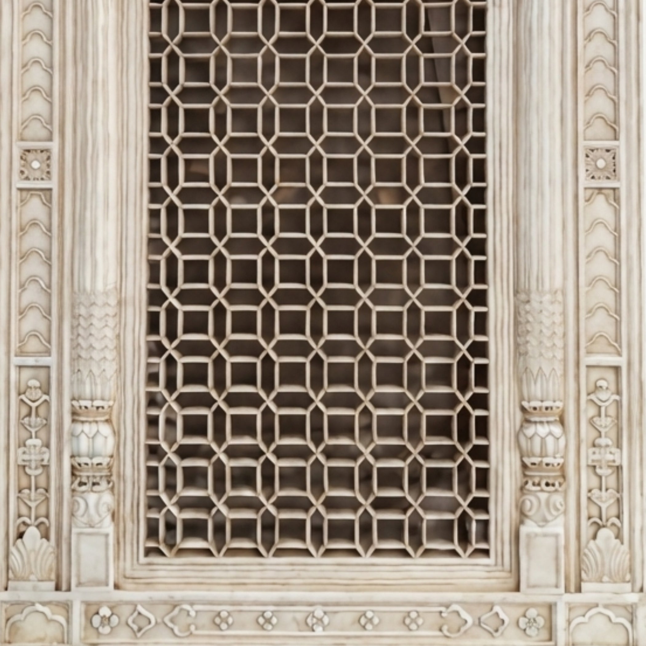 Close-up of an ornate carved stone window grille with a repeating geometric lattice pattern and decorative architectural framing.