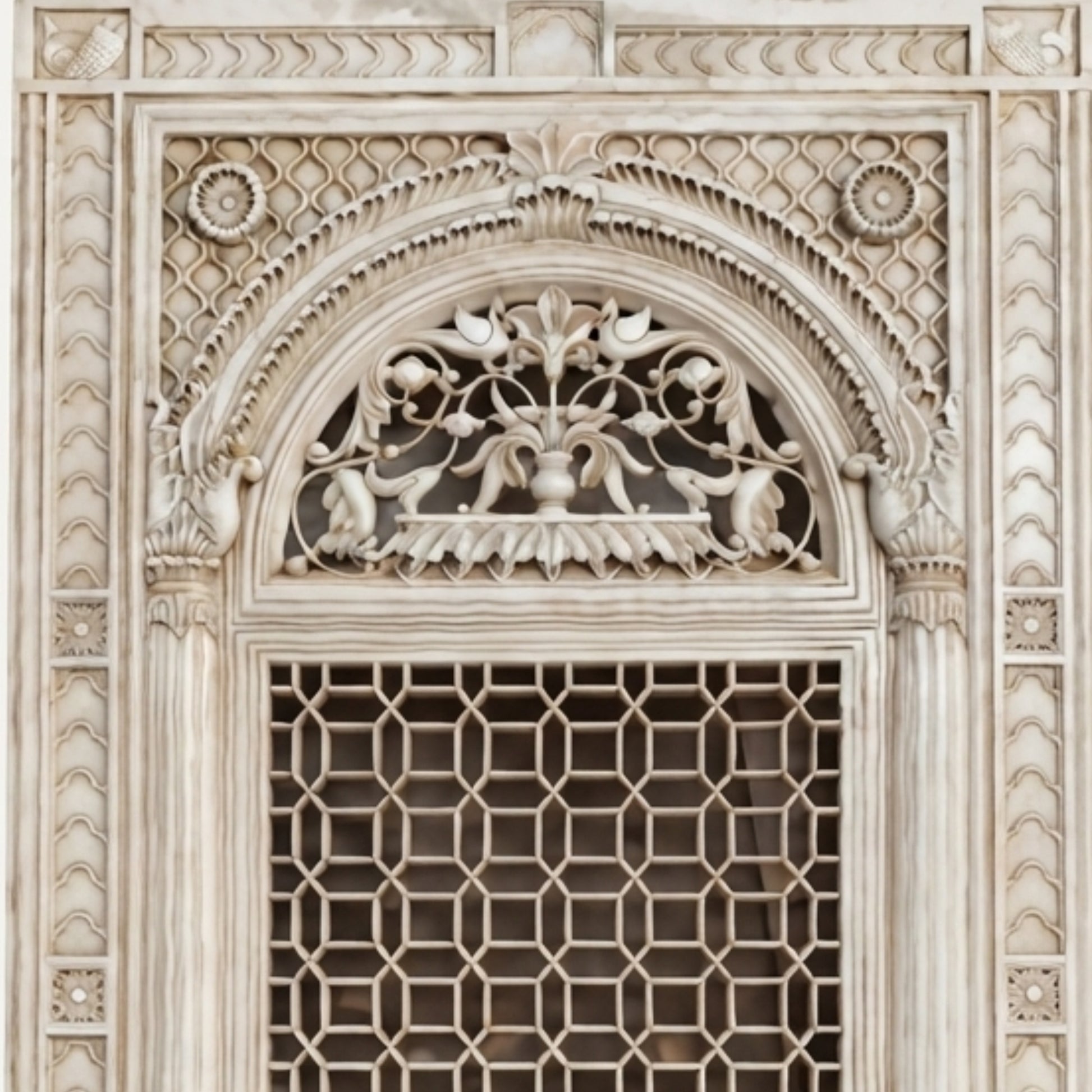 Close-up of an ornate carved stone window or door panel with a geometric lattice lower section and an arched decorative upper section featuring floral and bird motifs.